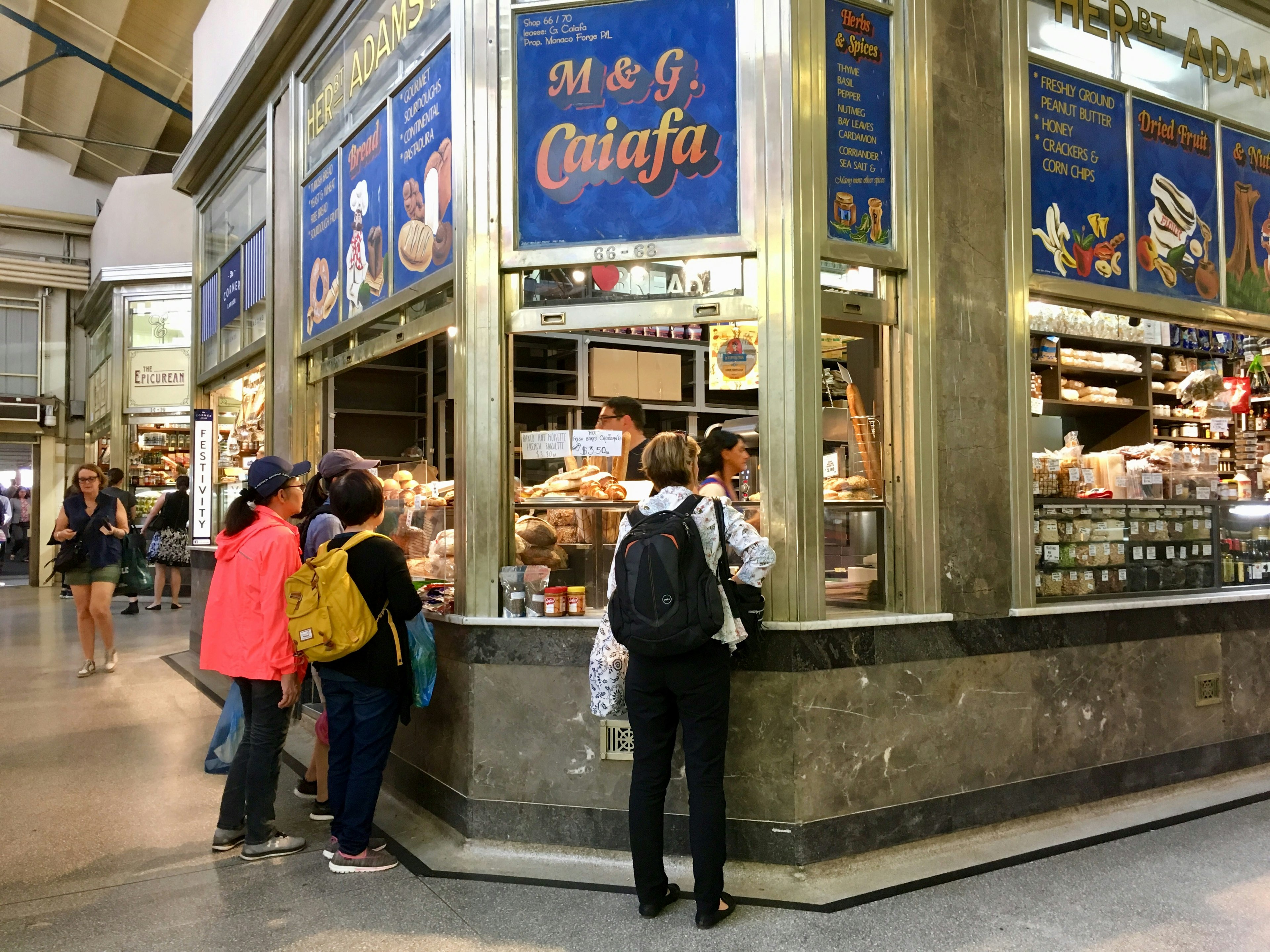 Customers buy pastries and other food goods from a stall in Queen Victoria Market, Melbourne