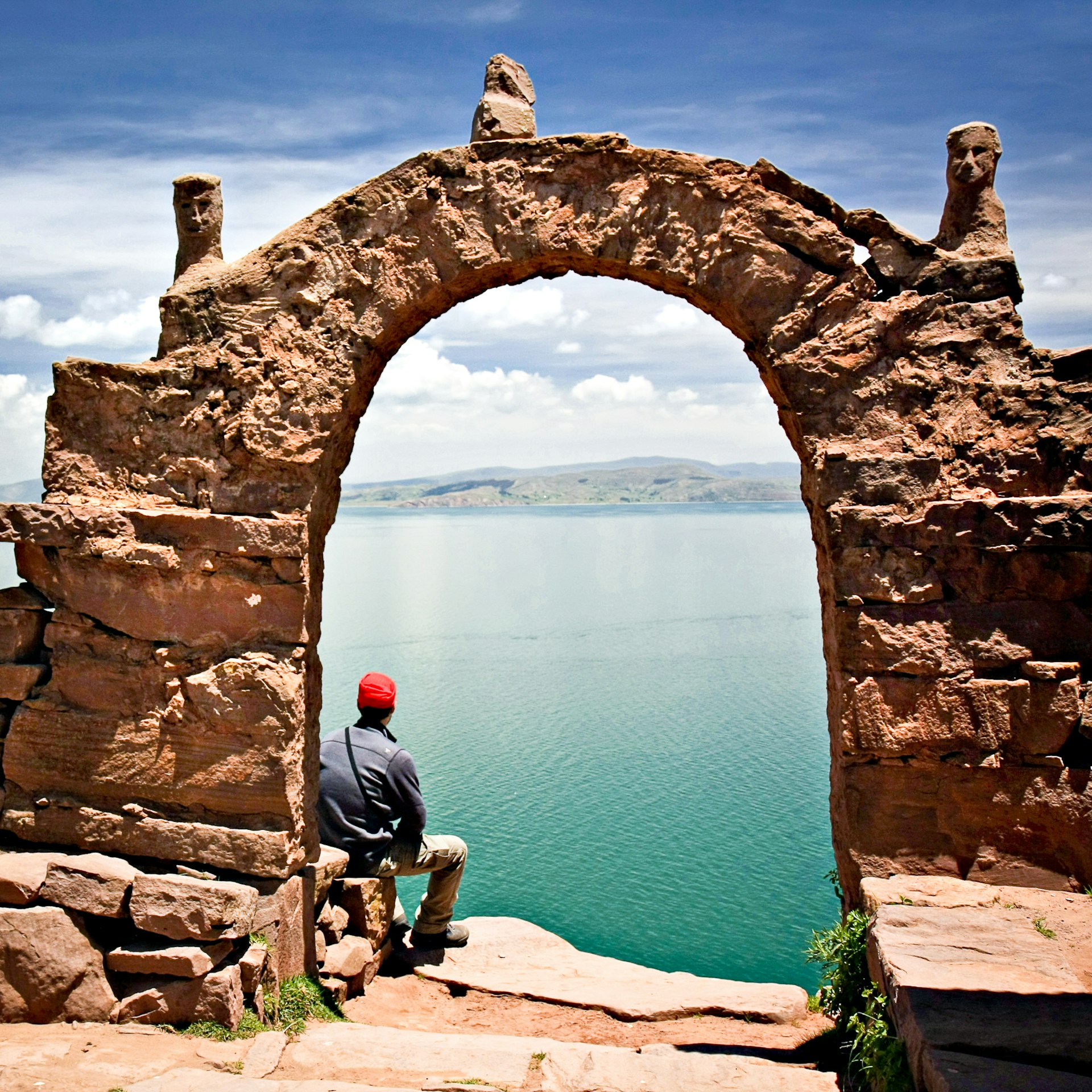 Man wearing a red hat, sits under a stone archway on Taquile Island, Lake Titicaca, Peru 