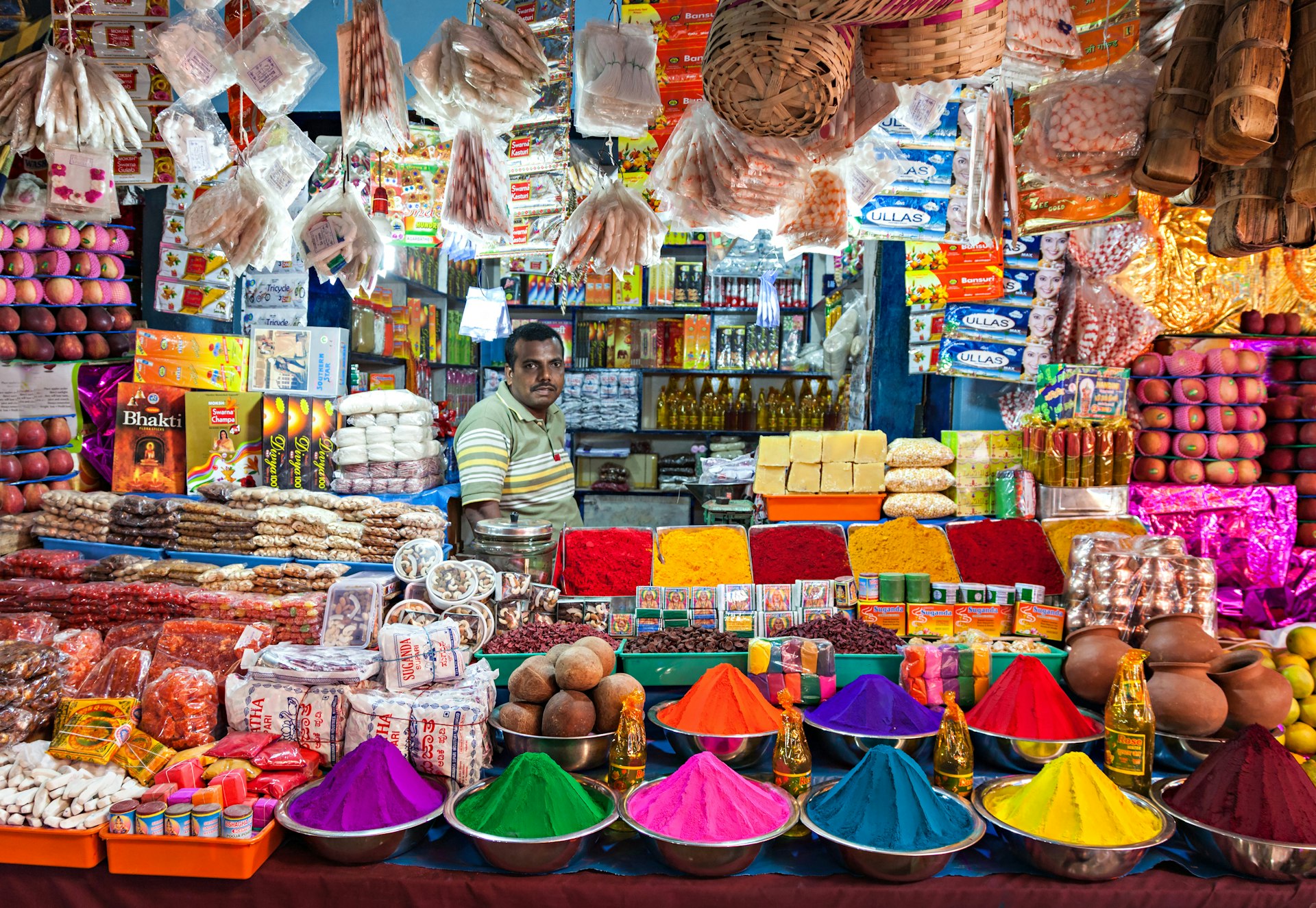 Man surrounded by colourful items at a small market stall in Delhi. 