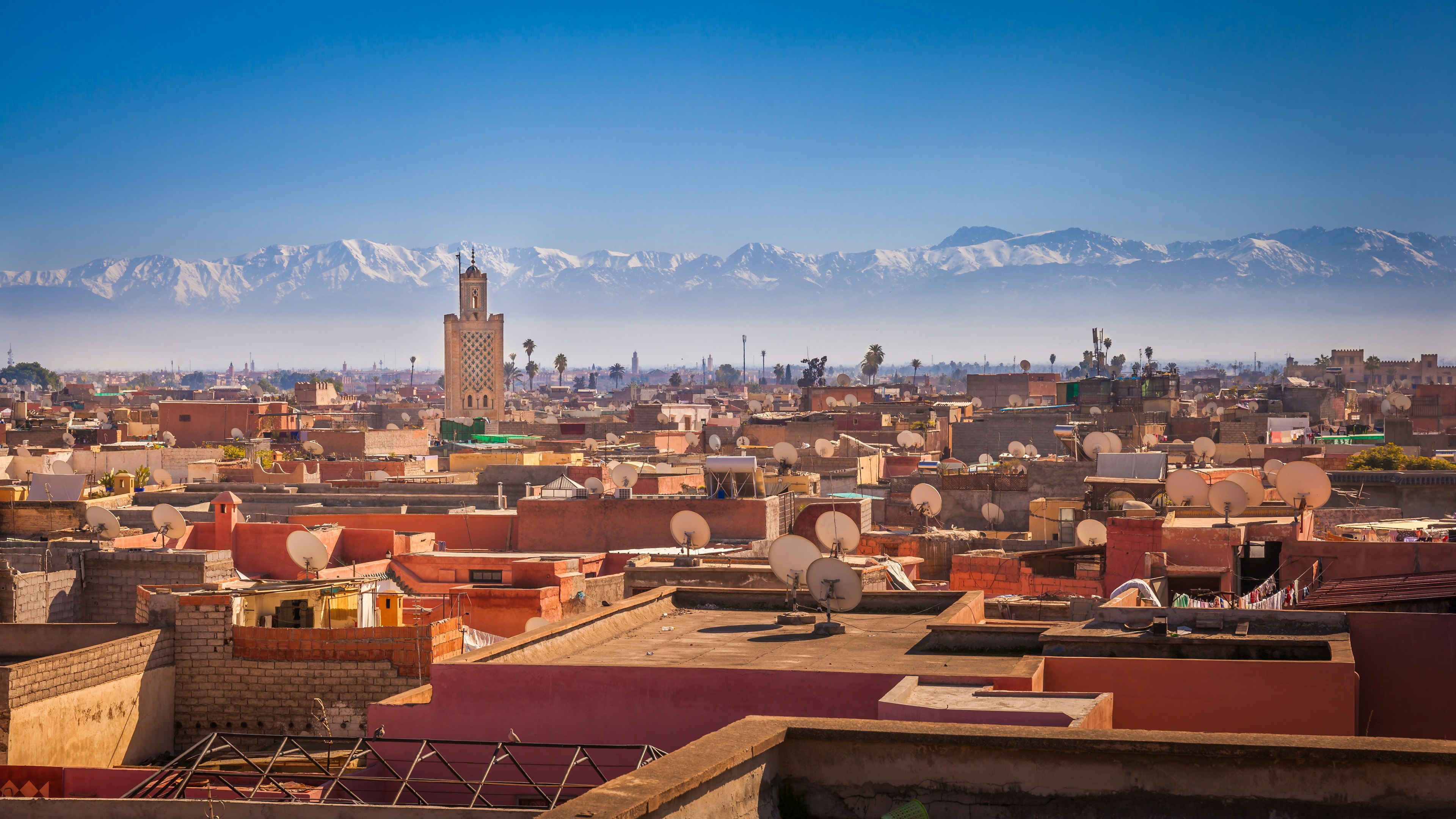 A view over red rooftops, dotted with satellite dishes, towards a vast mountain range on the horizon