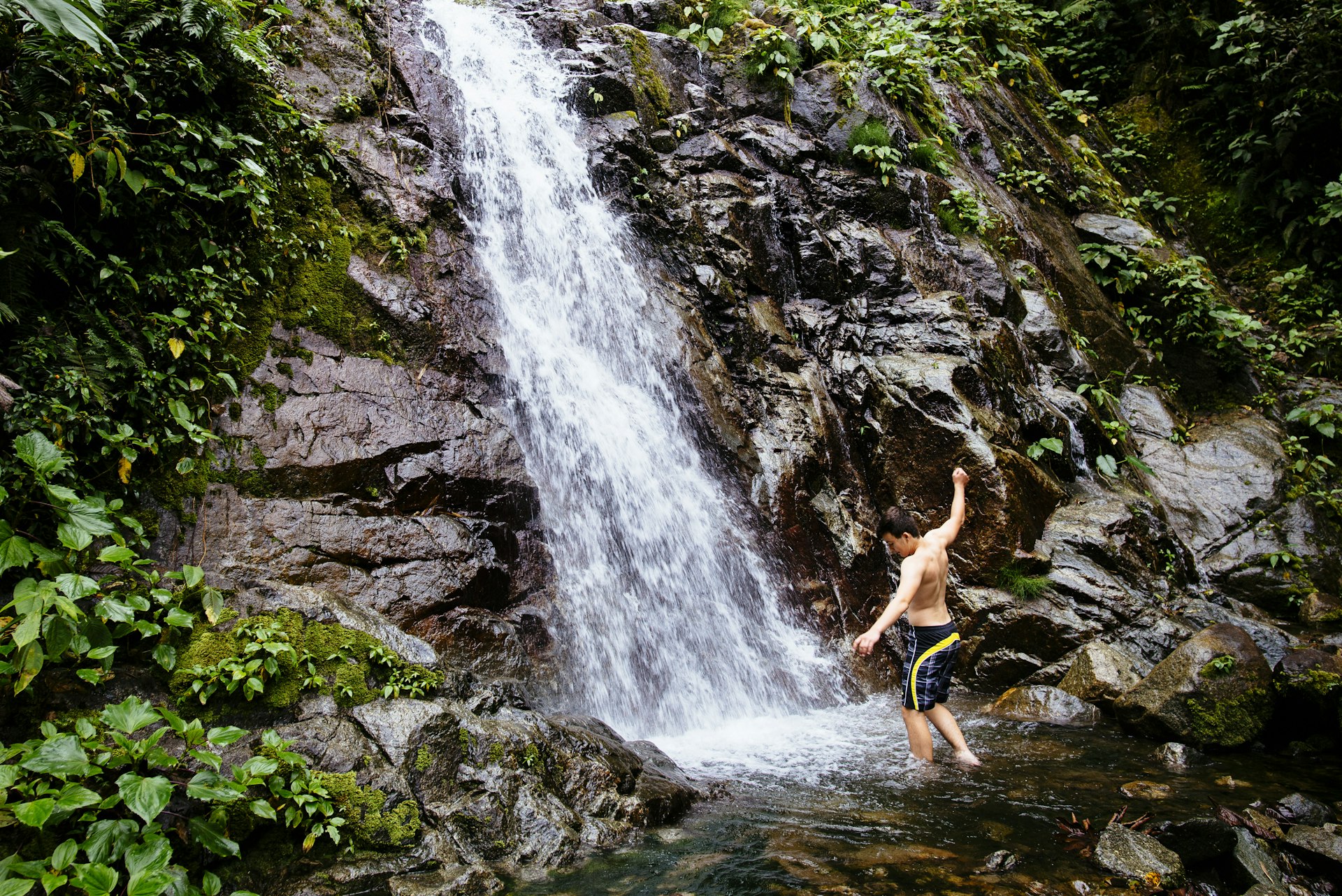 A young boy cools off under a waterfall