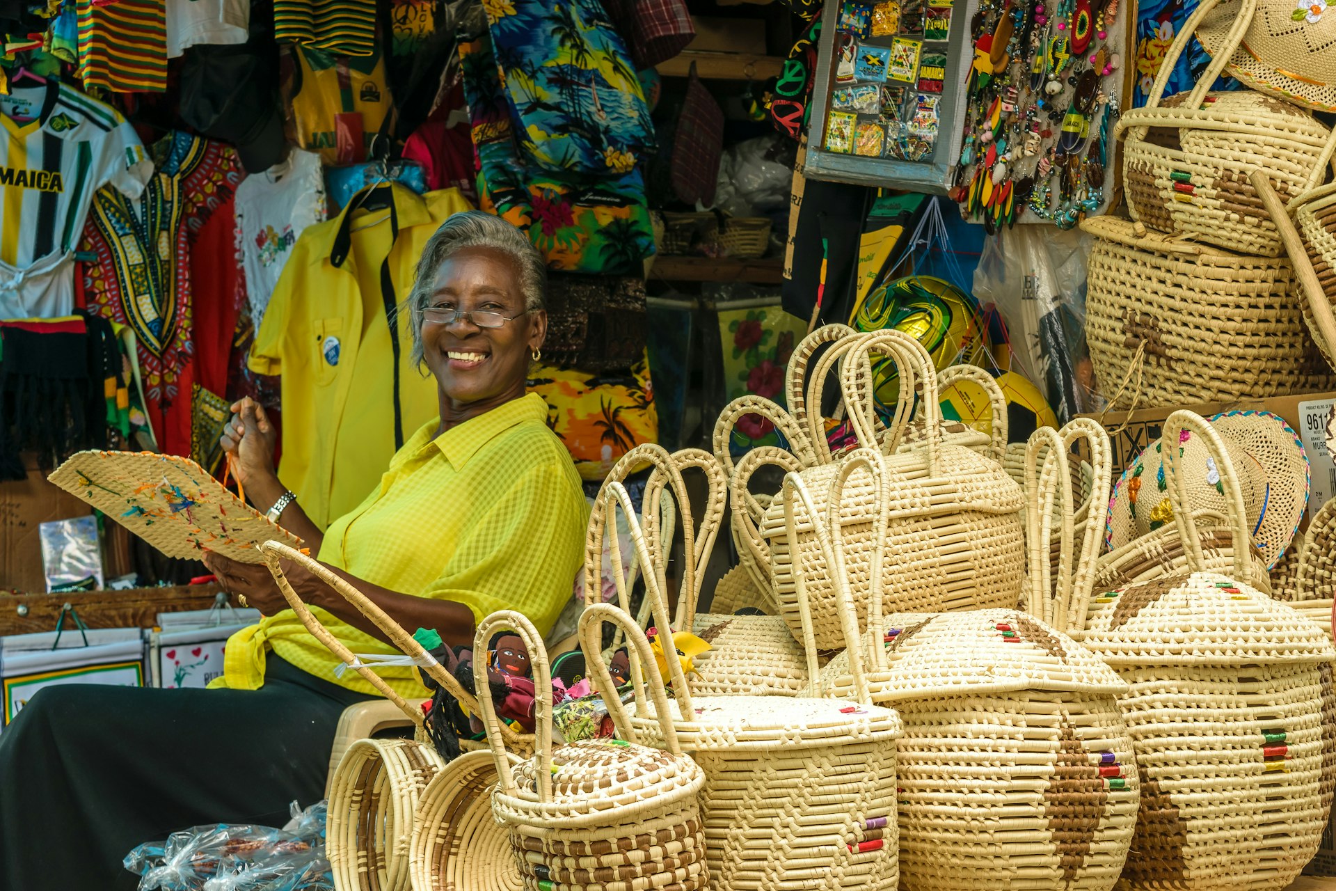 A woman smiles as she weaves baskets at her vendor stall in Montego Bay, Jamaica