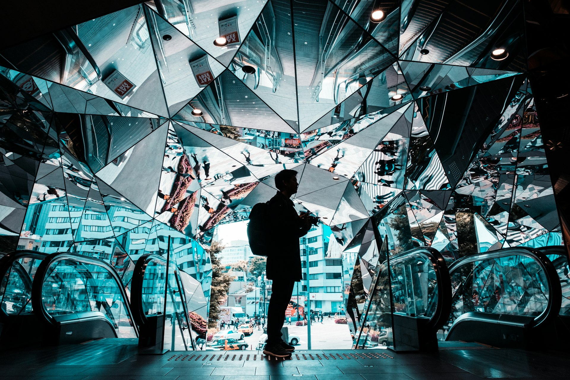 A man stands in the mirrored entrance of the Tokyo Plaza