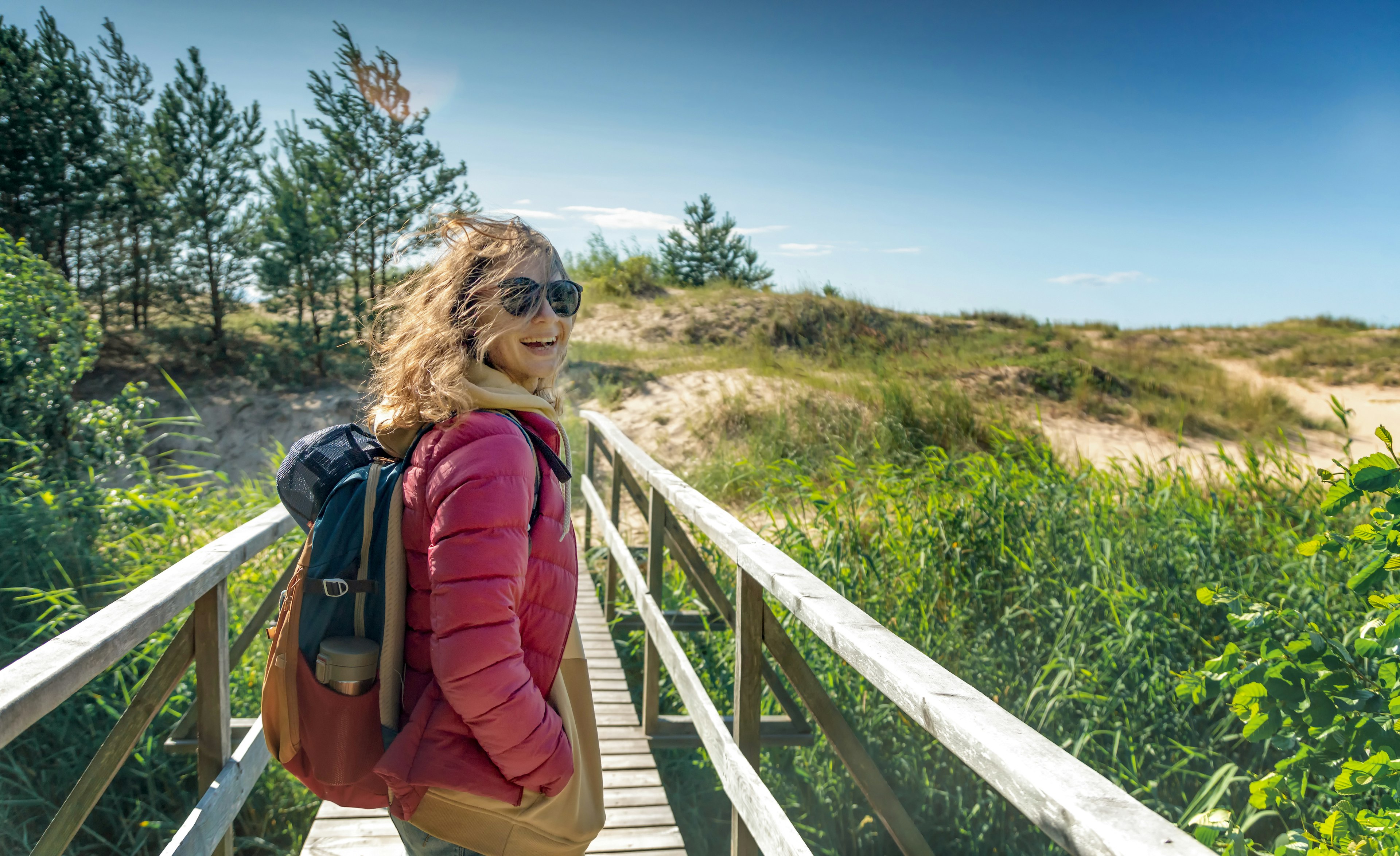 Young happy beautiful girl walks along the cold shore of the Baltic Sea in windy sunny weather.