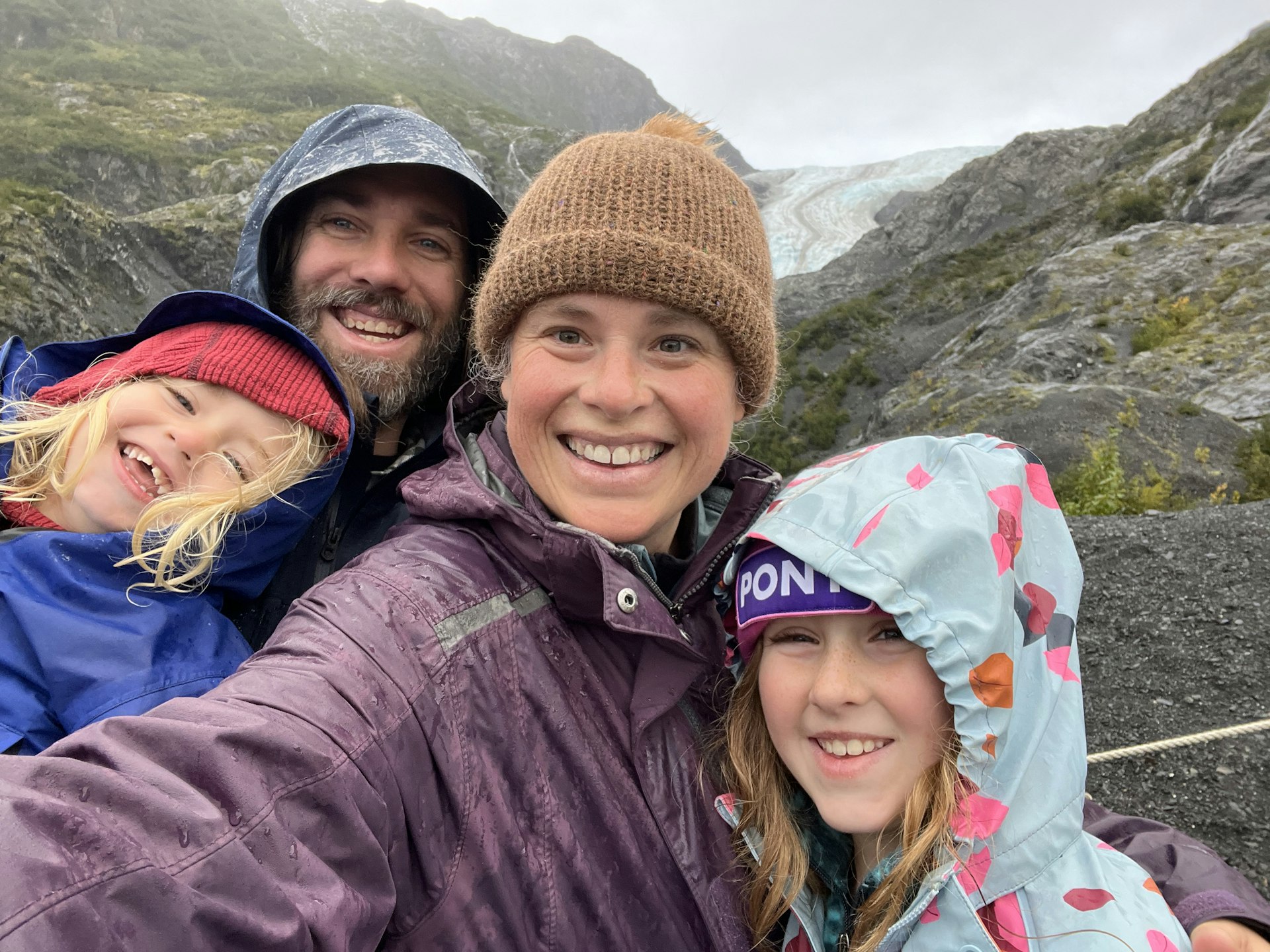 Sarah e sua família sorriem com roupas impermeáveis ​​depois de caminhar pelo Parque Nacional Kenai Fjords até a geleira Exit