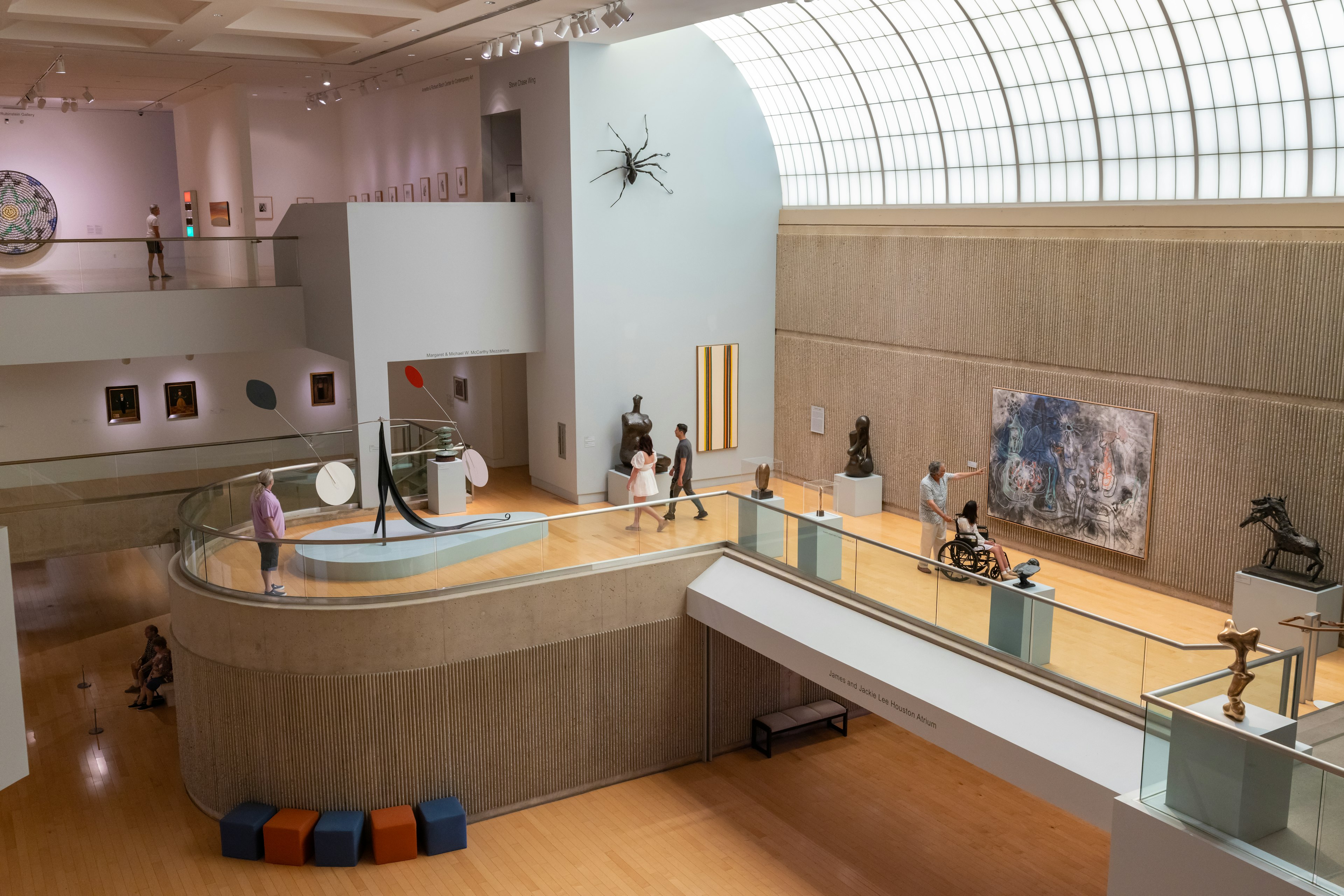 Patrons visit the Palm Springs Art Museum's main hall, where sculptures and paitings line the walls and sunlight comes down through a curved glass skylight.