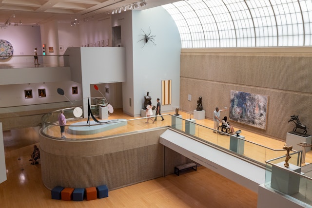 Patrons visit the Palm Springs Art Museum's main hall, where sculptures and paitings line the walls and sunlight comes down through a curved glass skylight.