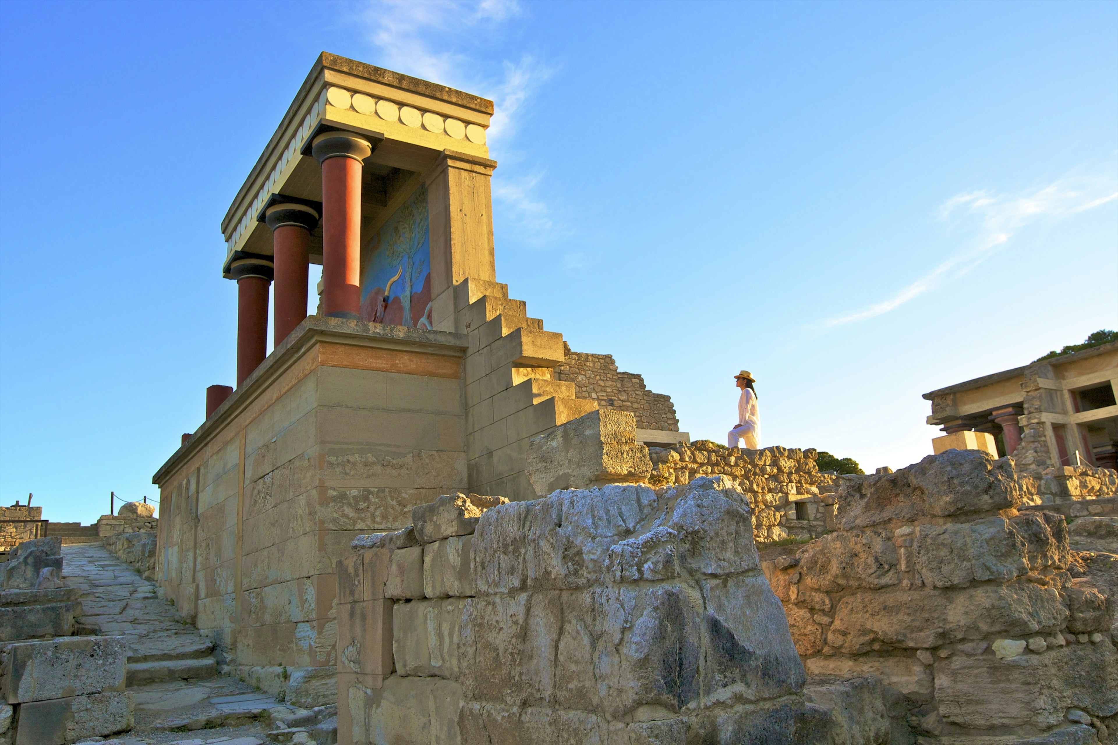 A woman walks up stairs to the ruins of a temple-like building covered in delicate paintings