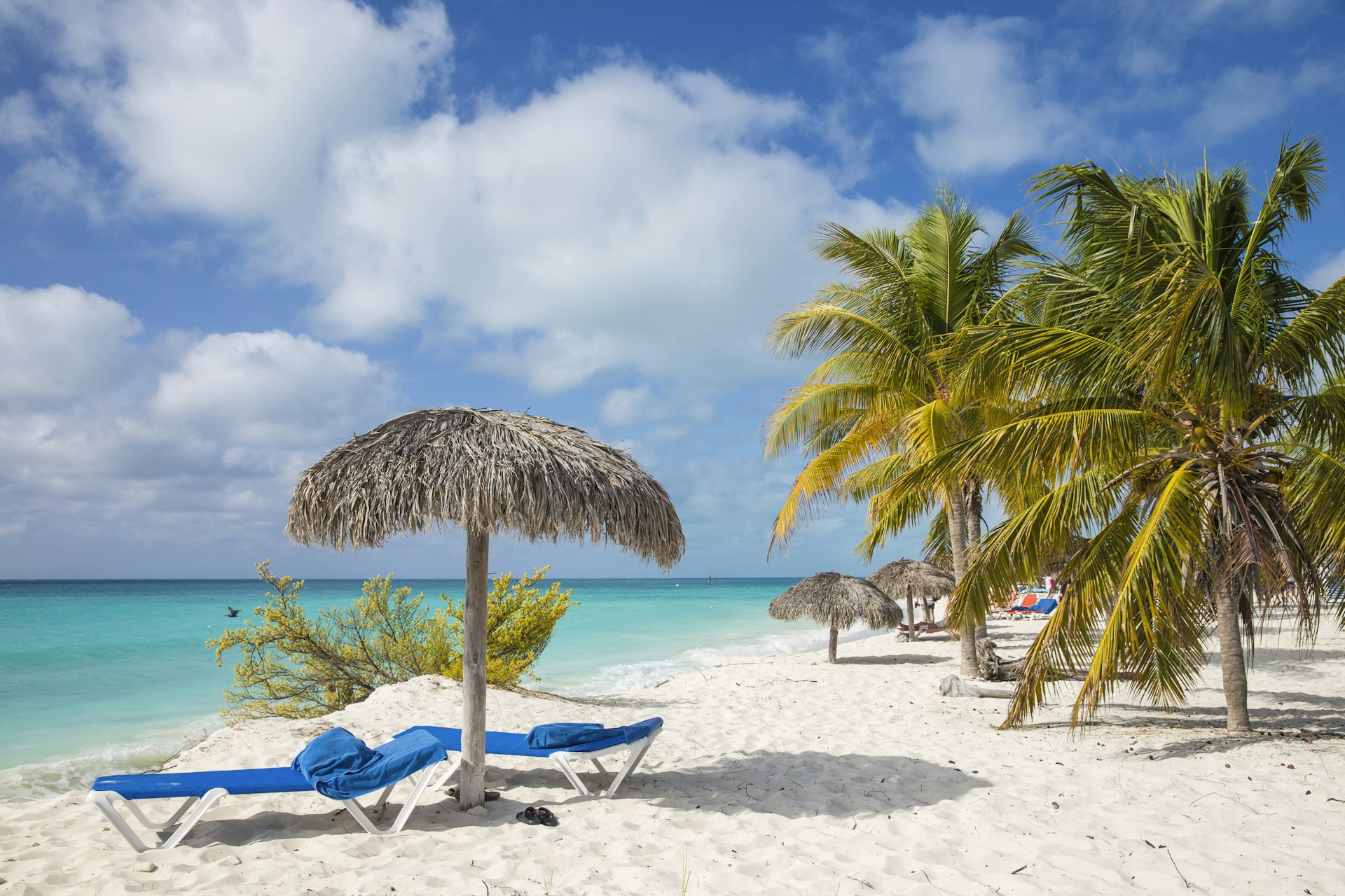 A few beach loungers are arranged under a palm tree parasol on the white-sand beach of Playa Isla de la Juventud, Cuba