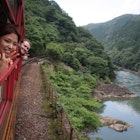 A woman and a man lean out of train windows and smile as they travel through Kyoto, Japan