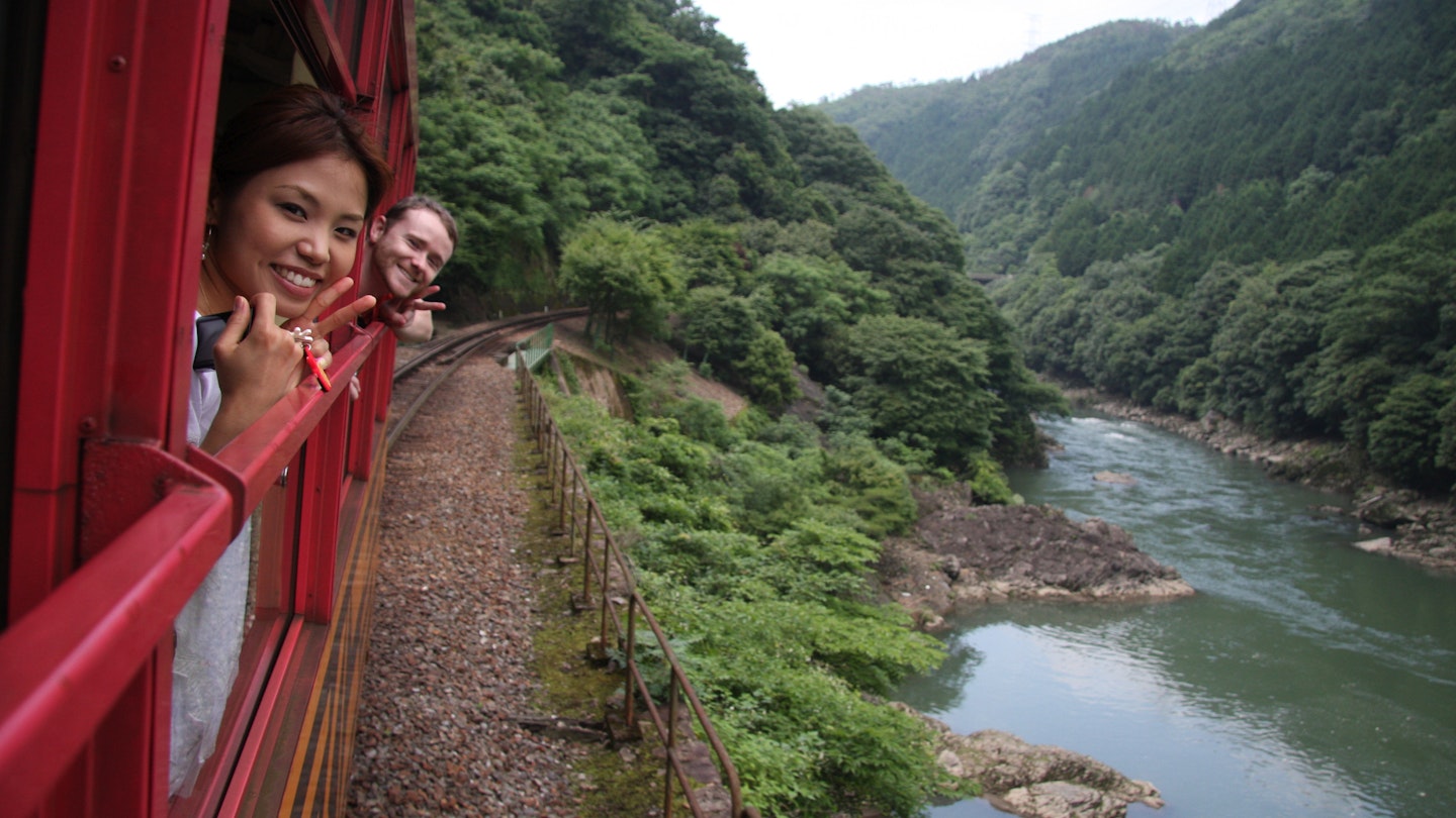 A woman and a man lean out of train windows and smile as they travel through Kyoto, Japan