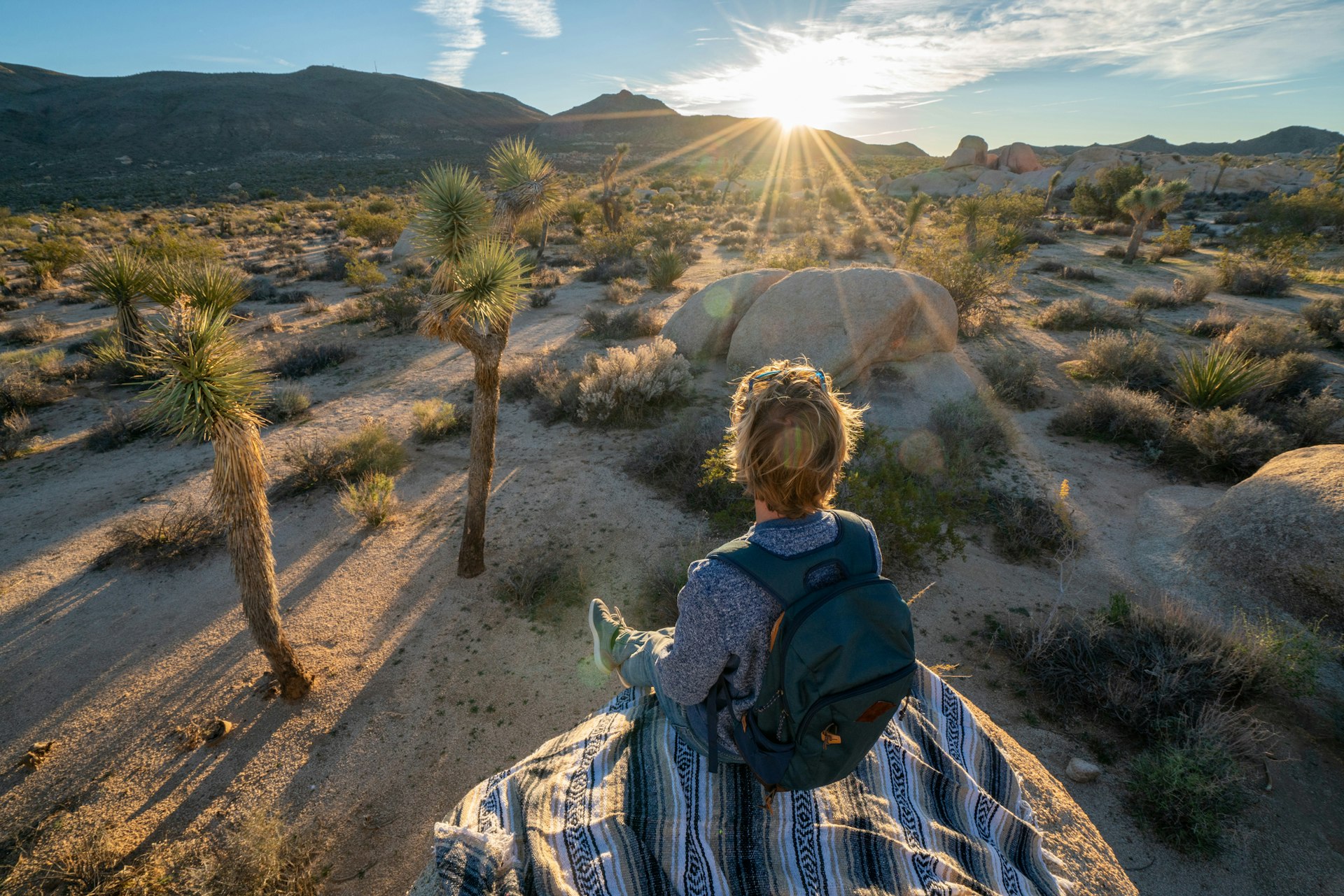 A young traveler in Joshua Tree National Park, USA, contemplating the sun rising from behind a rock formation
