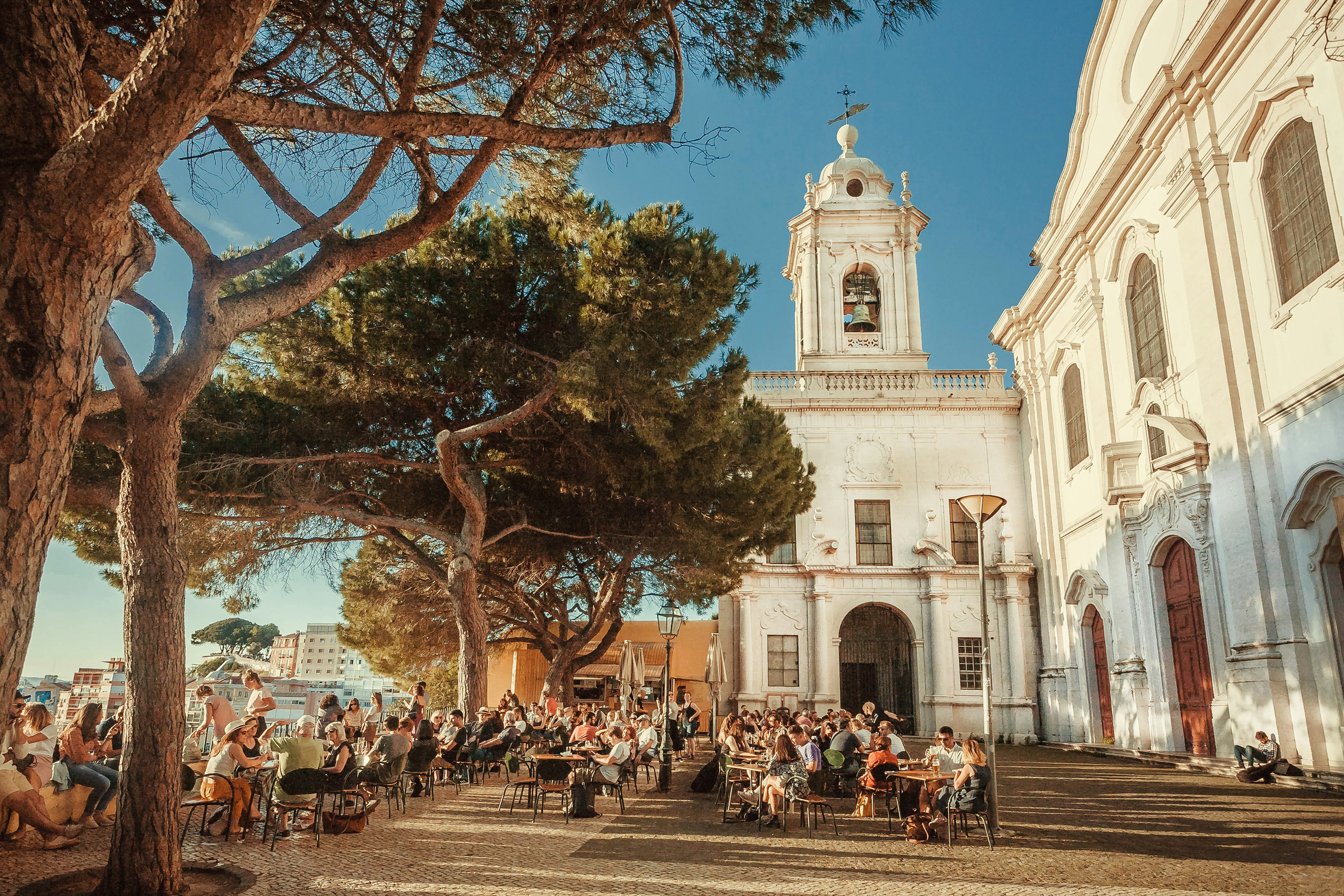 Crowd of visitors of outdoor restaurant drinking and relaxing on terrace with beautiful city view in Alfama, Lisbon