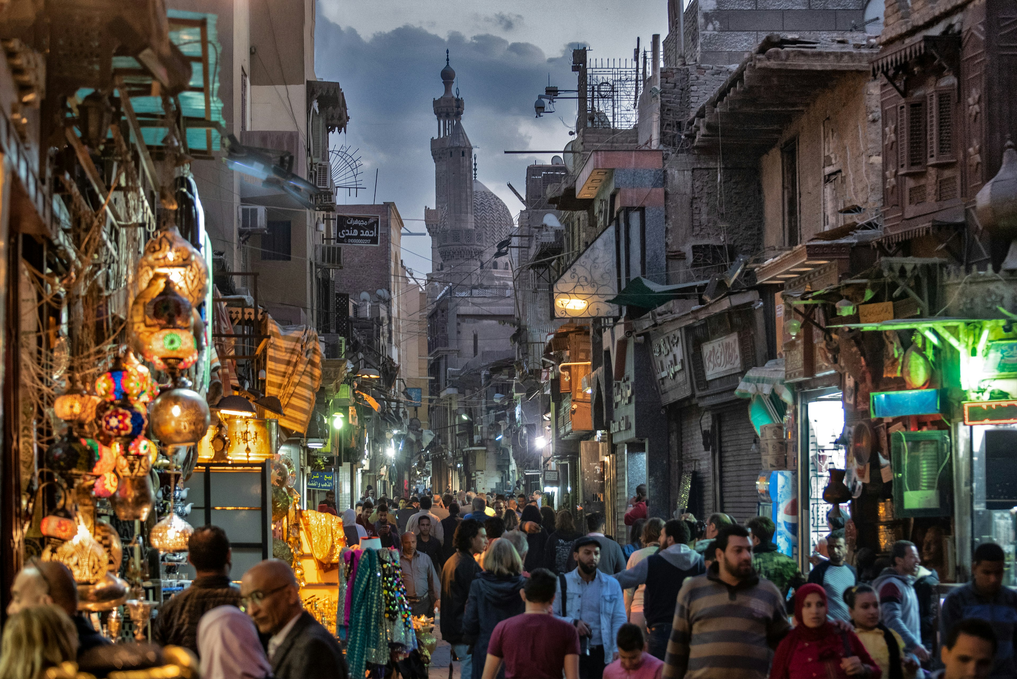 Crowds on a pedestrianized street during the late afternoon. There's a large mosque at one end.