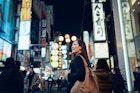 Smiling young Asian female traveller exploring and strolling along the busy and colourful neon signboard downtown city street at night in Osaka, Japan
1202888936