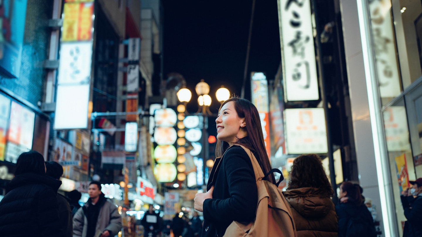 Smiling young Asian female traveller exploring and strolling along the busy and colourful neon signboard downtown city street at night in Osaka, Japan
1202888936