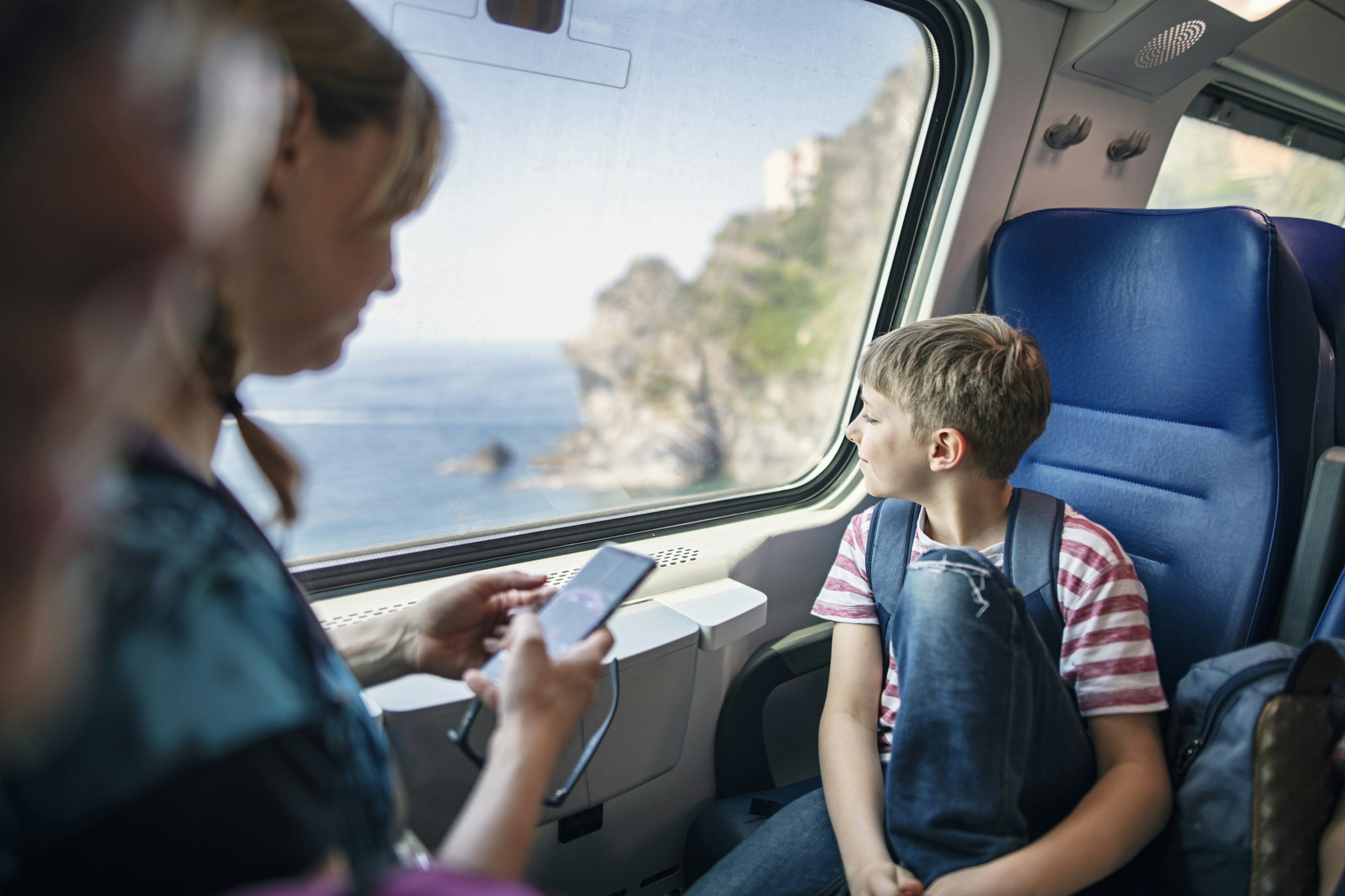 Mother and son tourists travelling by train between towns in Cinque Terre, Italy. The son is looking at beautiful landscapes