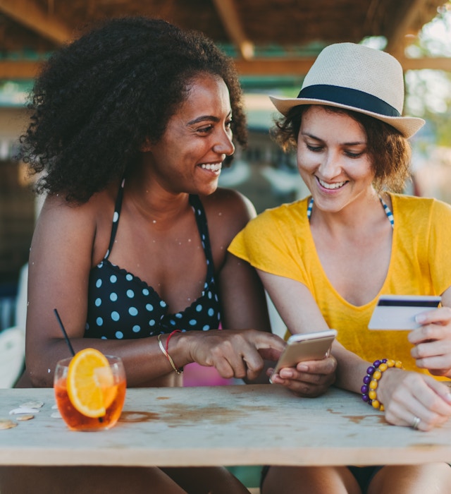 Happy women on beach holiday shopping online - stock photo
Smiling women drinking cocktails at the veranda and shopping online