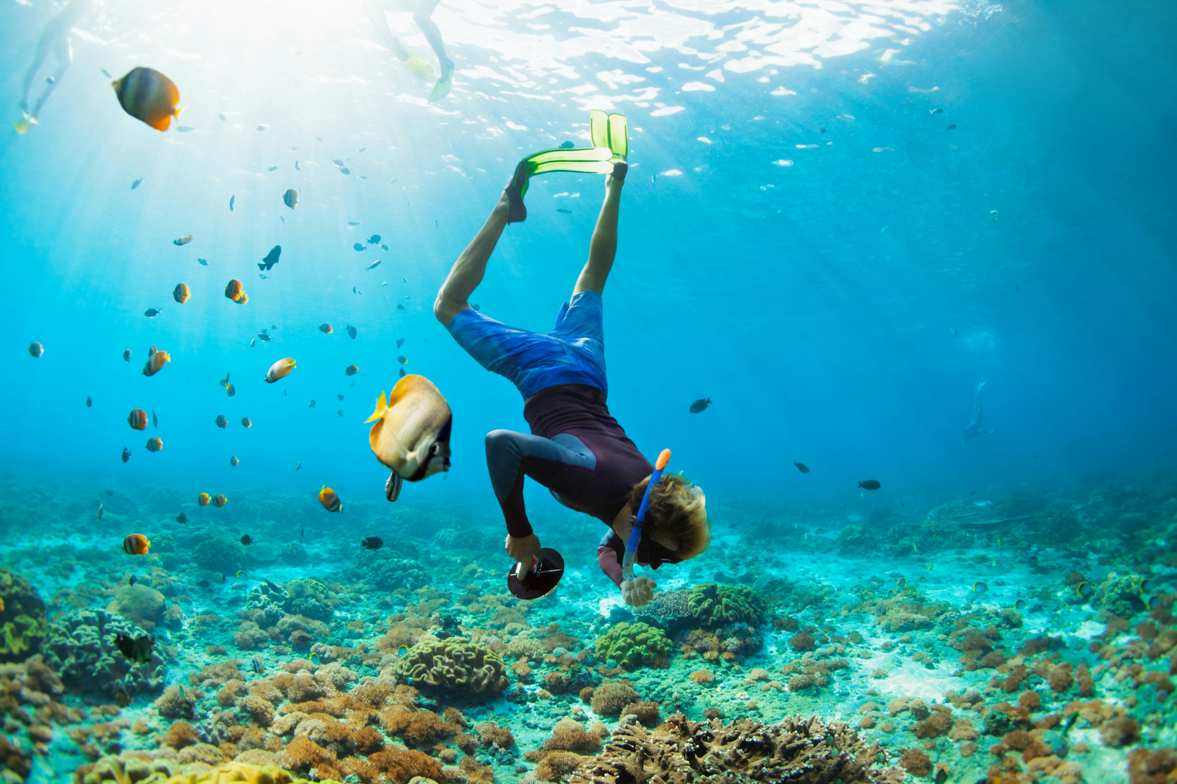 Man in snorkeling mask with camera dive underwater with tropical fishes in coral reef sea pool