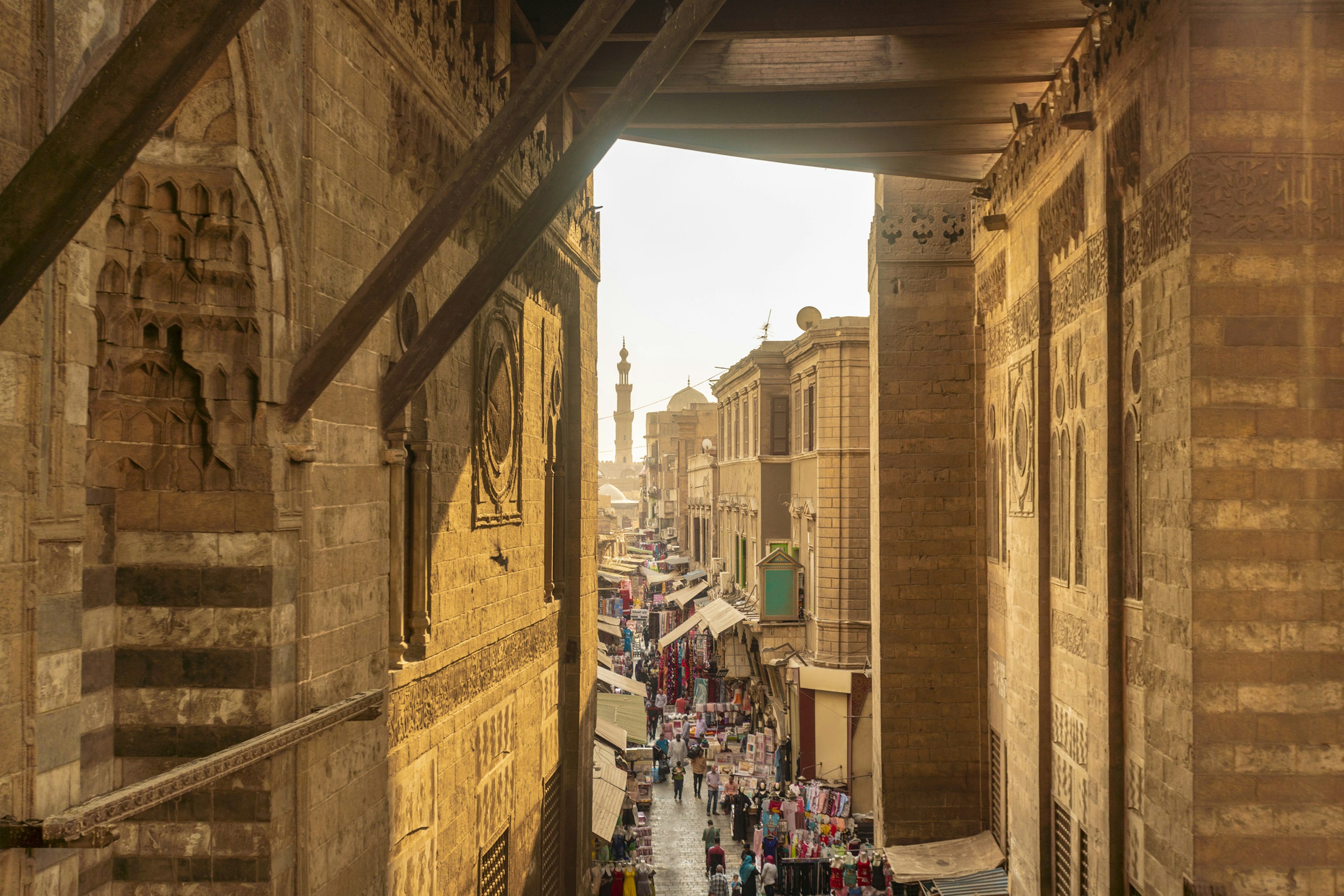 People walk down a busy market street in a city