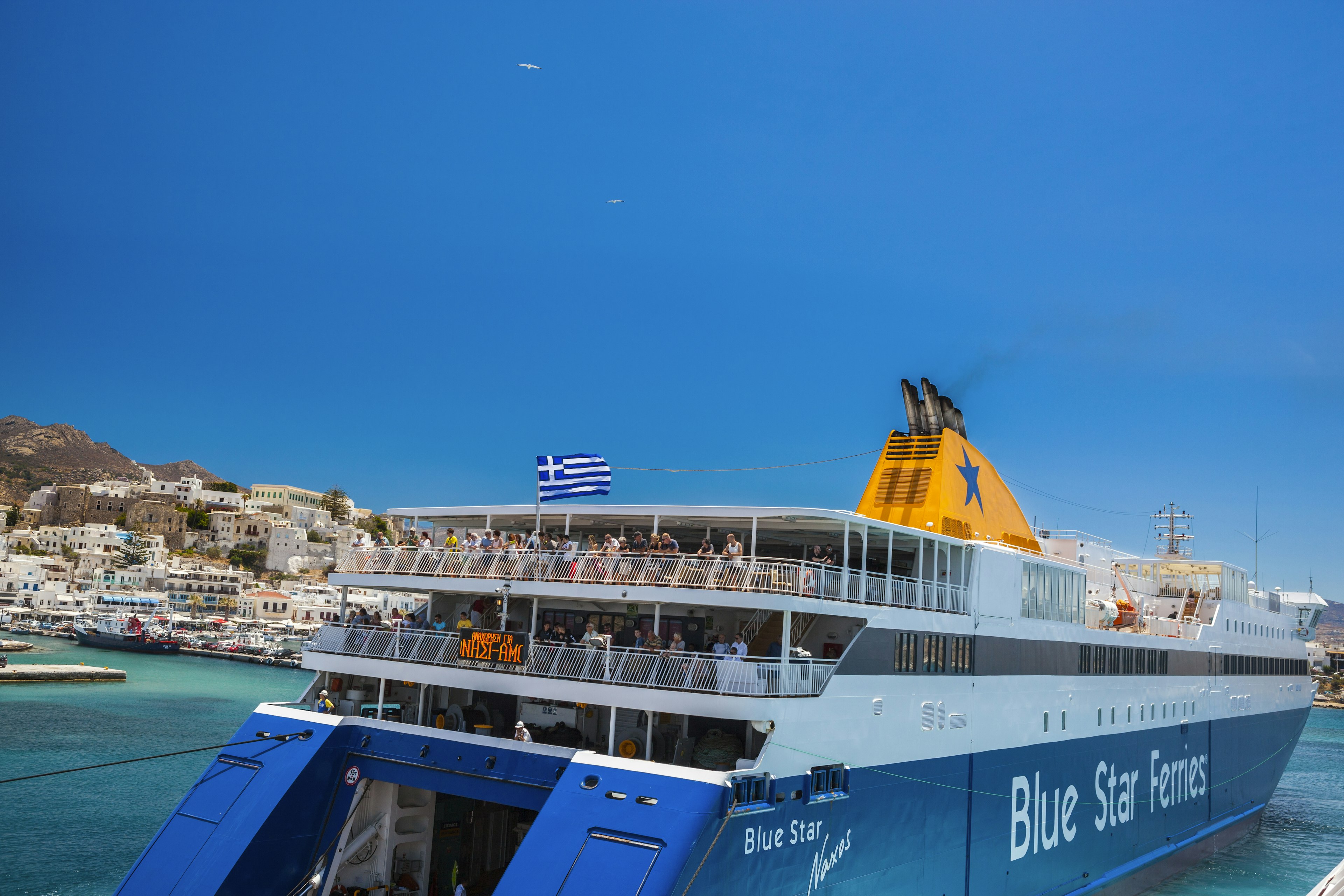 This is the port of Naxos with boats, cars, stores, restaurants. You can see  people in the Blue Star Naxos Ferry and is boarding travelers.