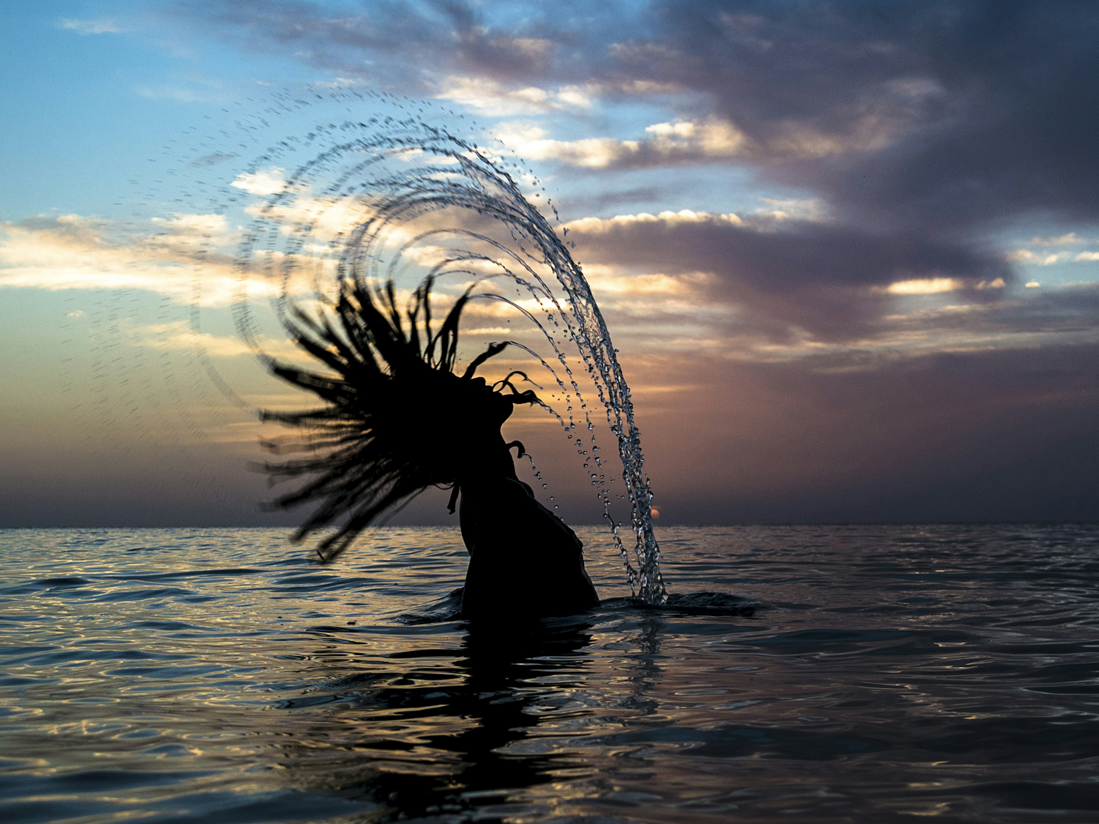 A young woman wetting and flipping her hair in the sea during a sunset in Jamaica