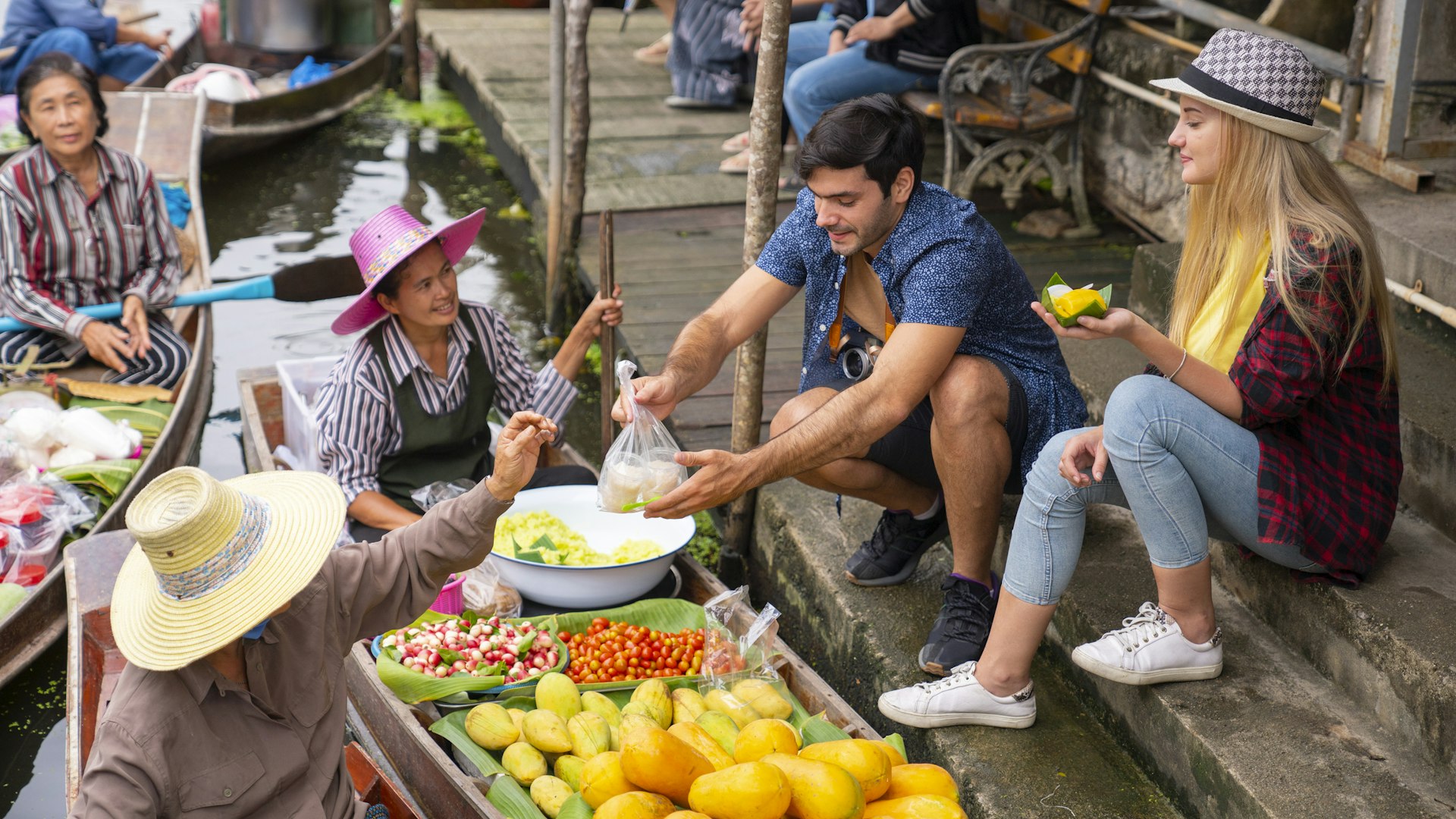 Two tourists buy produce from a vendor whose stall is a boat on a canal