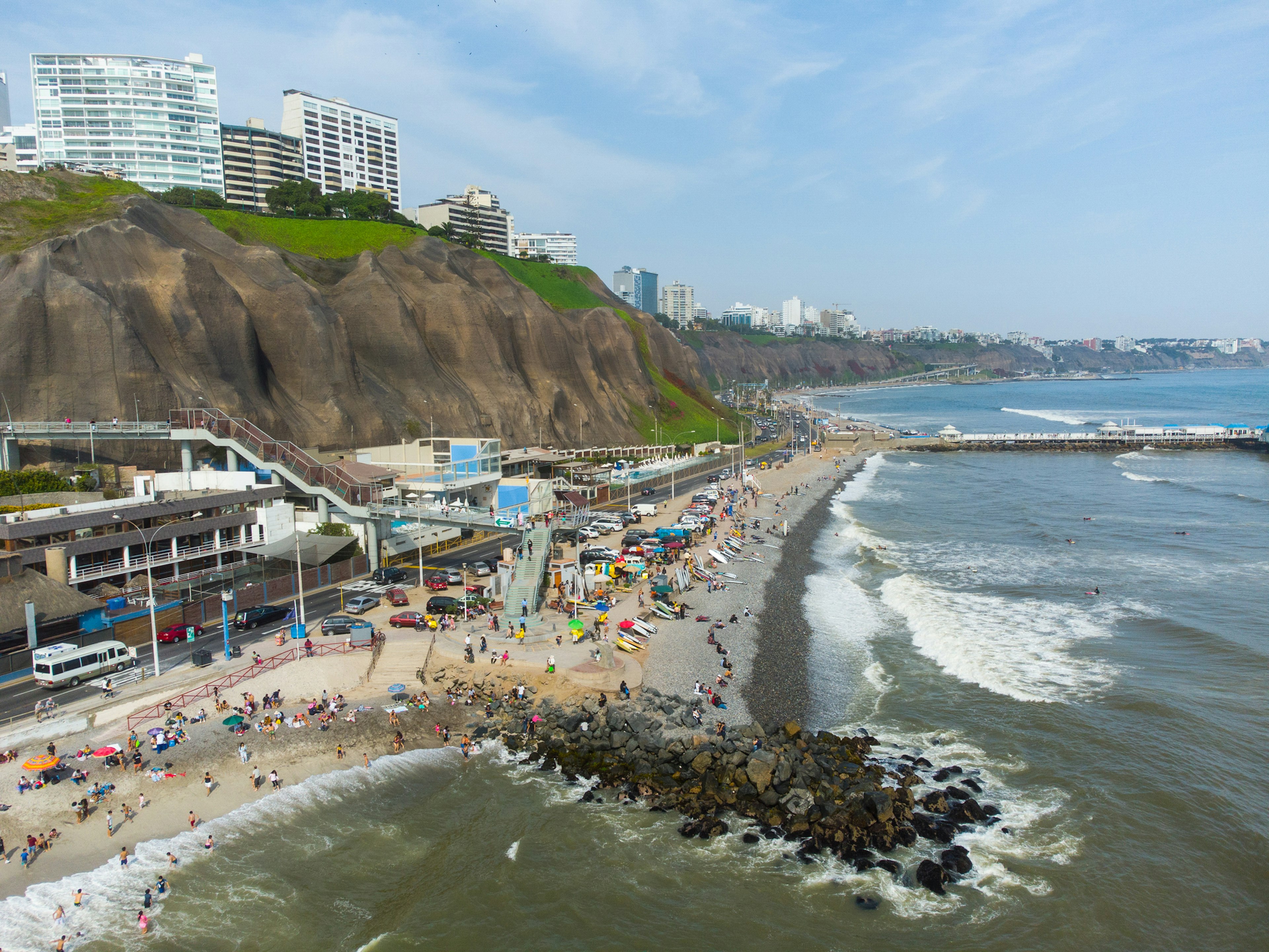 People sunbathe and surf off a beach backed by high cliffs