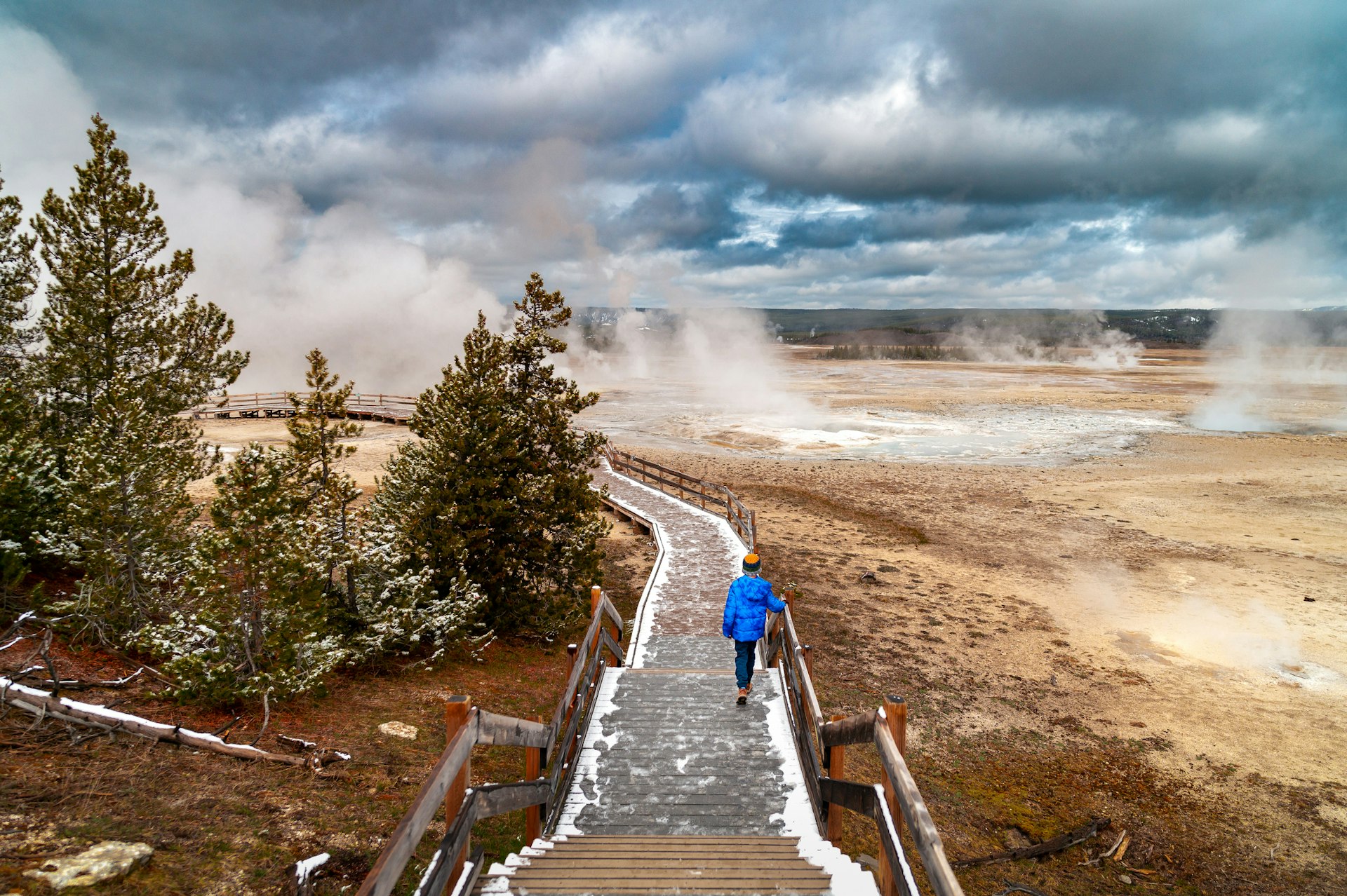 A man in hiking gear walks along a wooden walkway around the steaming geyser at Yellowstone National Park