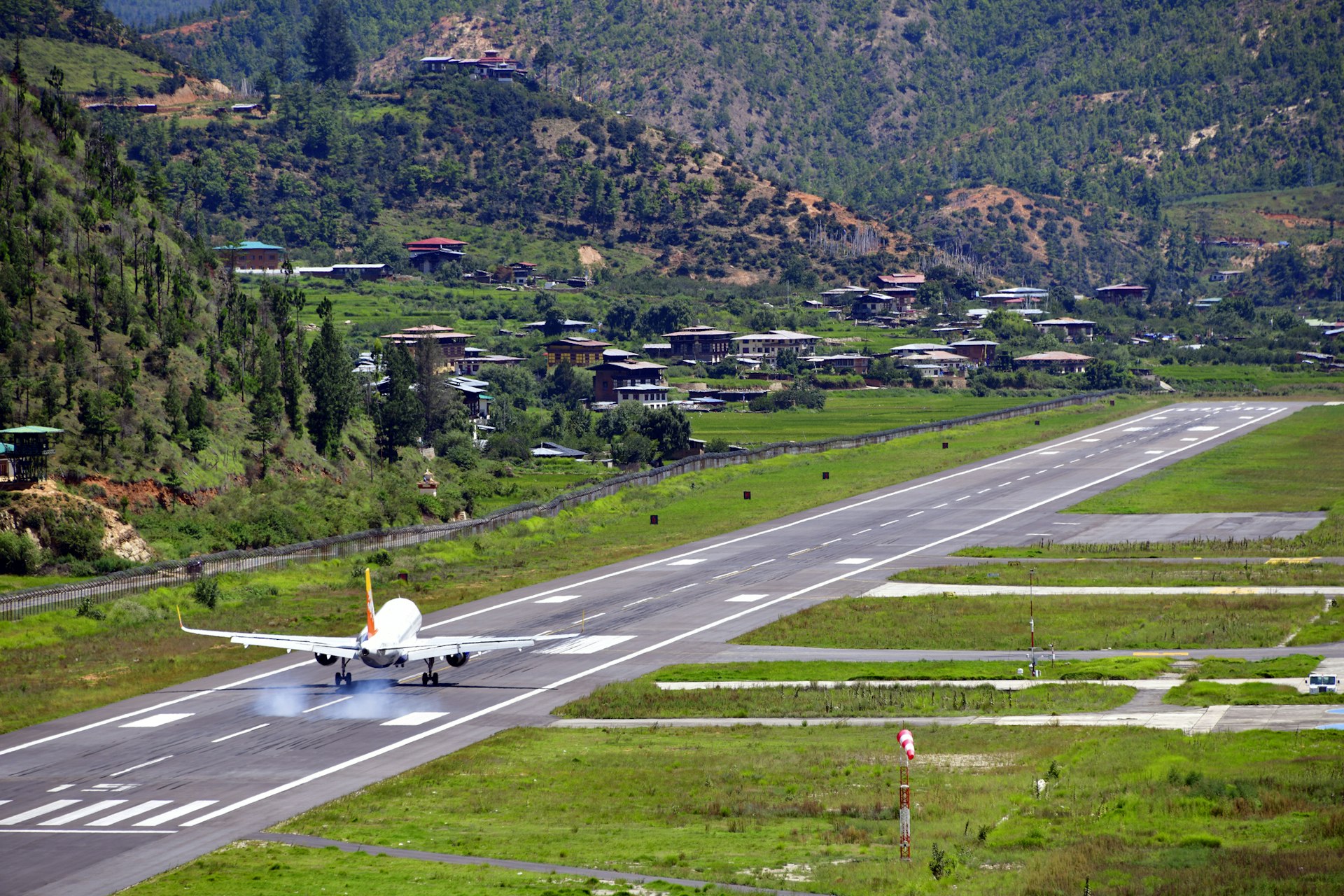 A plan lands on a runways surrounded by steep green hillsides 