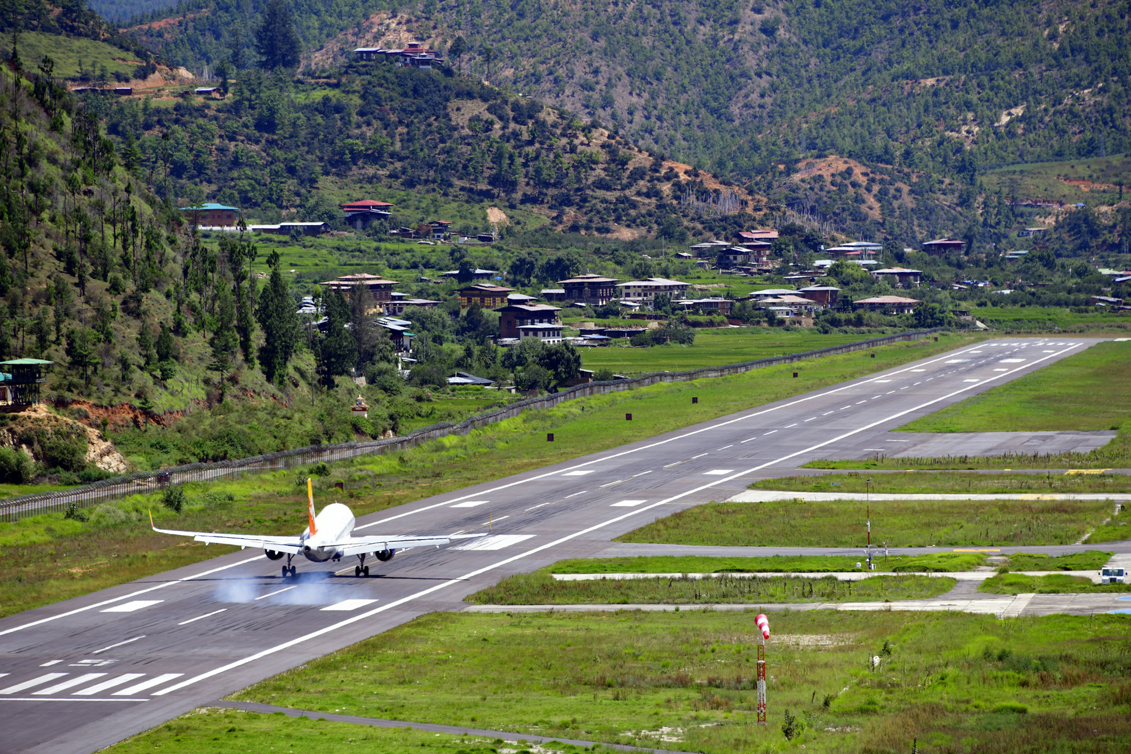 A plane lands on a runway surrounded by steep green hillsides