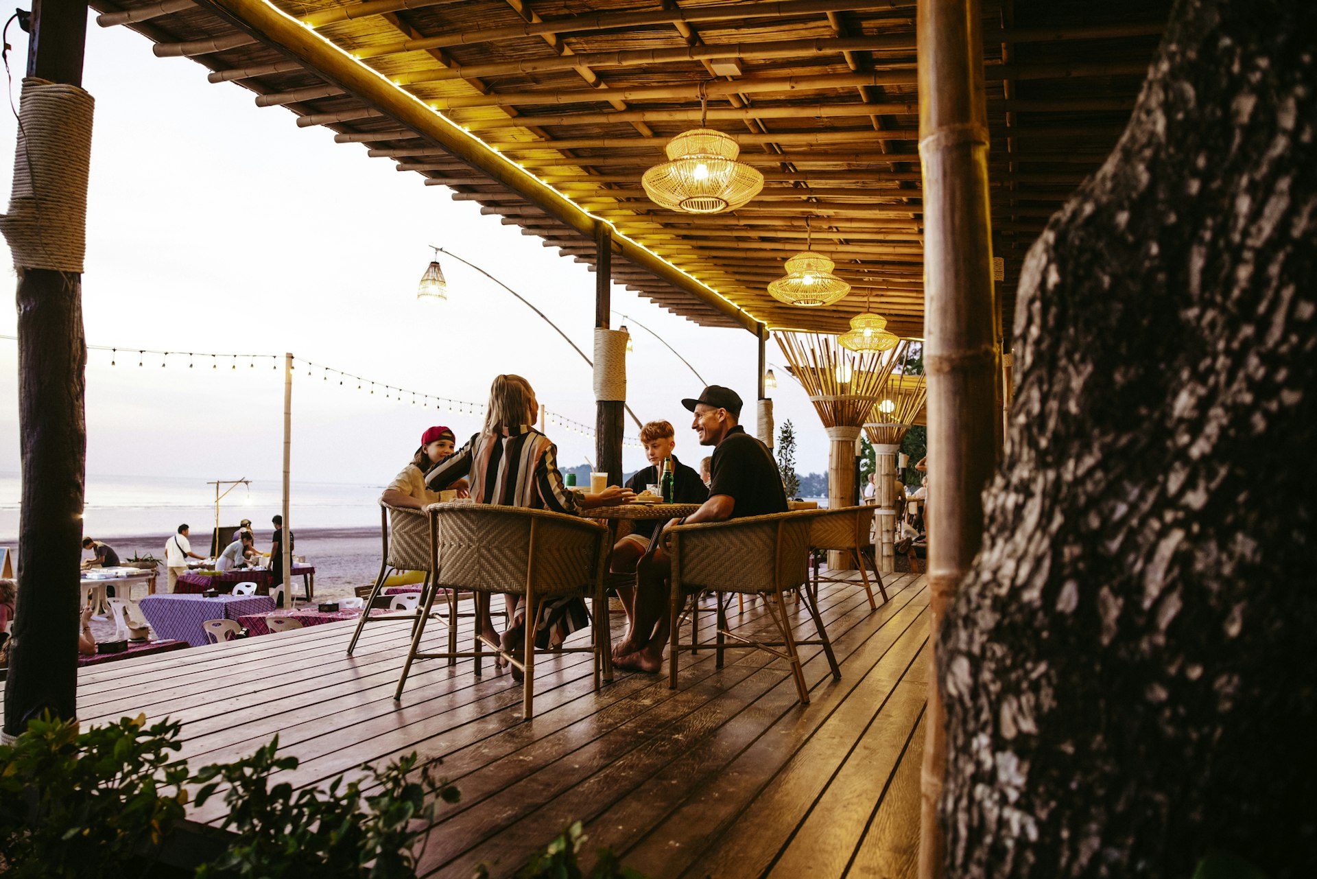 A family of four sit at a table in a beachside restaurant