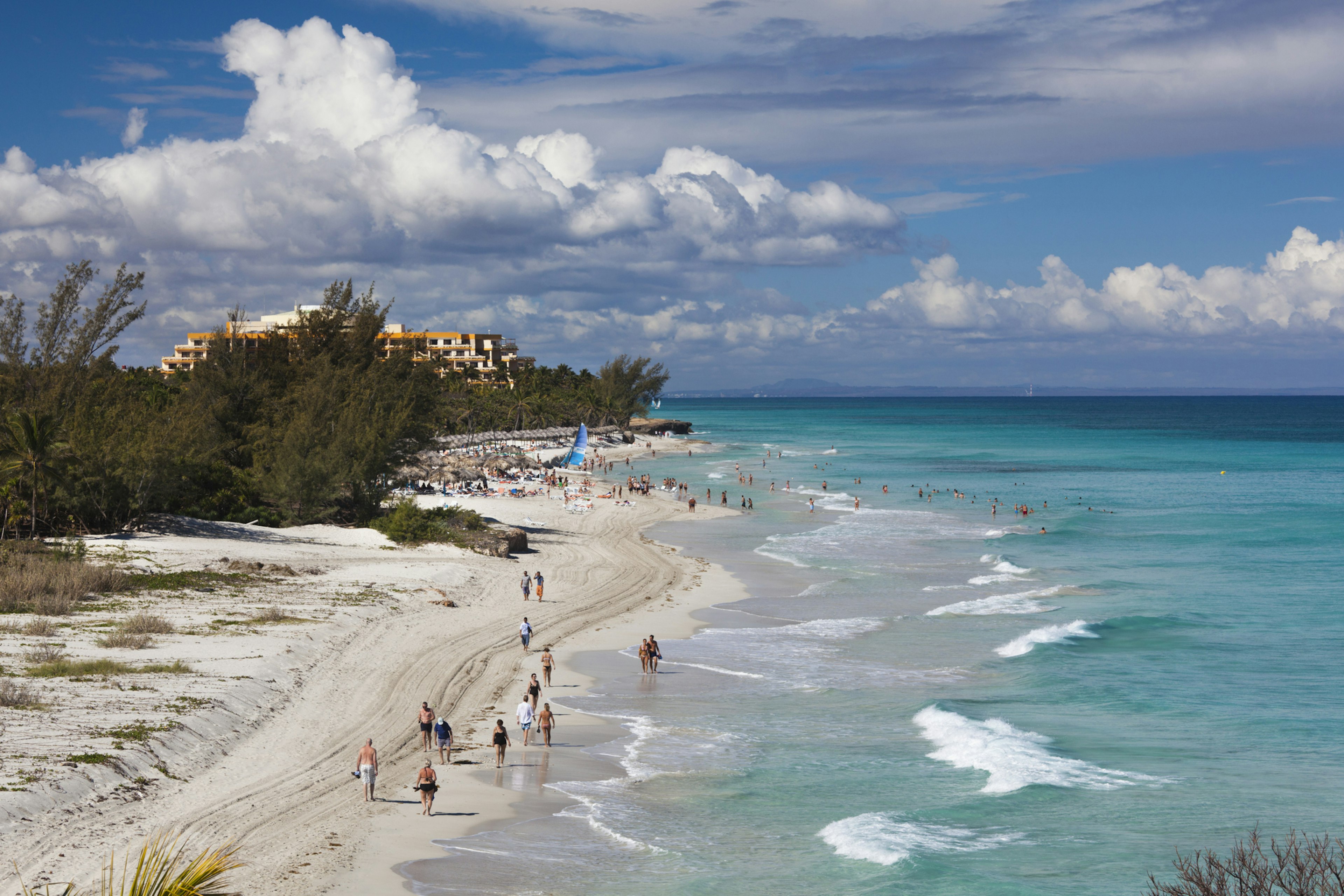 A beautiful white-sand beach backed by a hotel. Lots of people take up space on the sand near the building