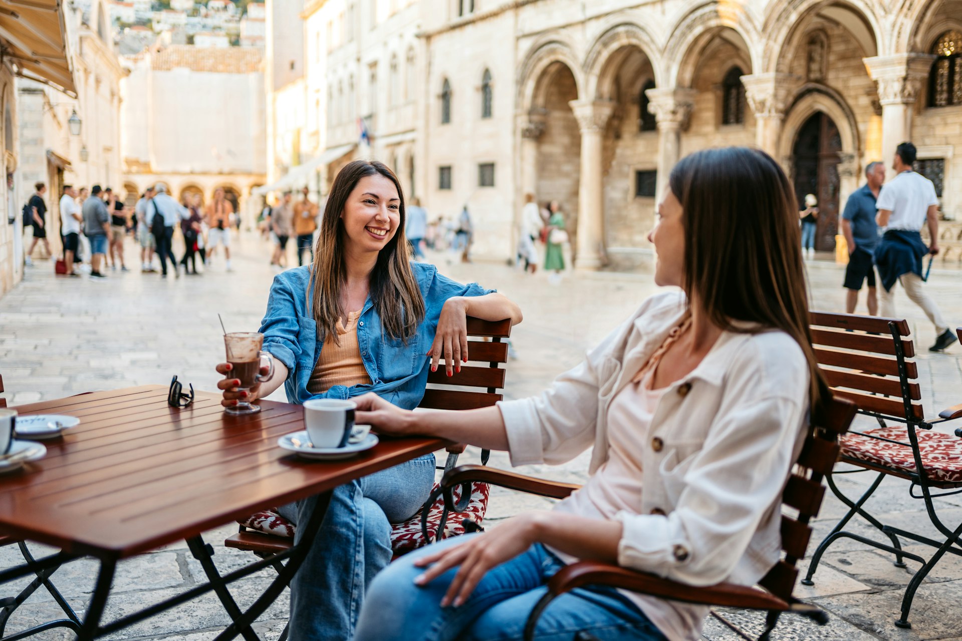 Two young female friends drinking coffee in a sidewalk café in Dubrovnik, Croatia