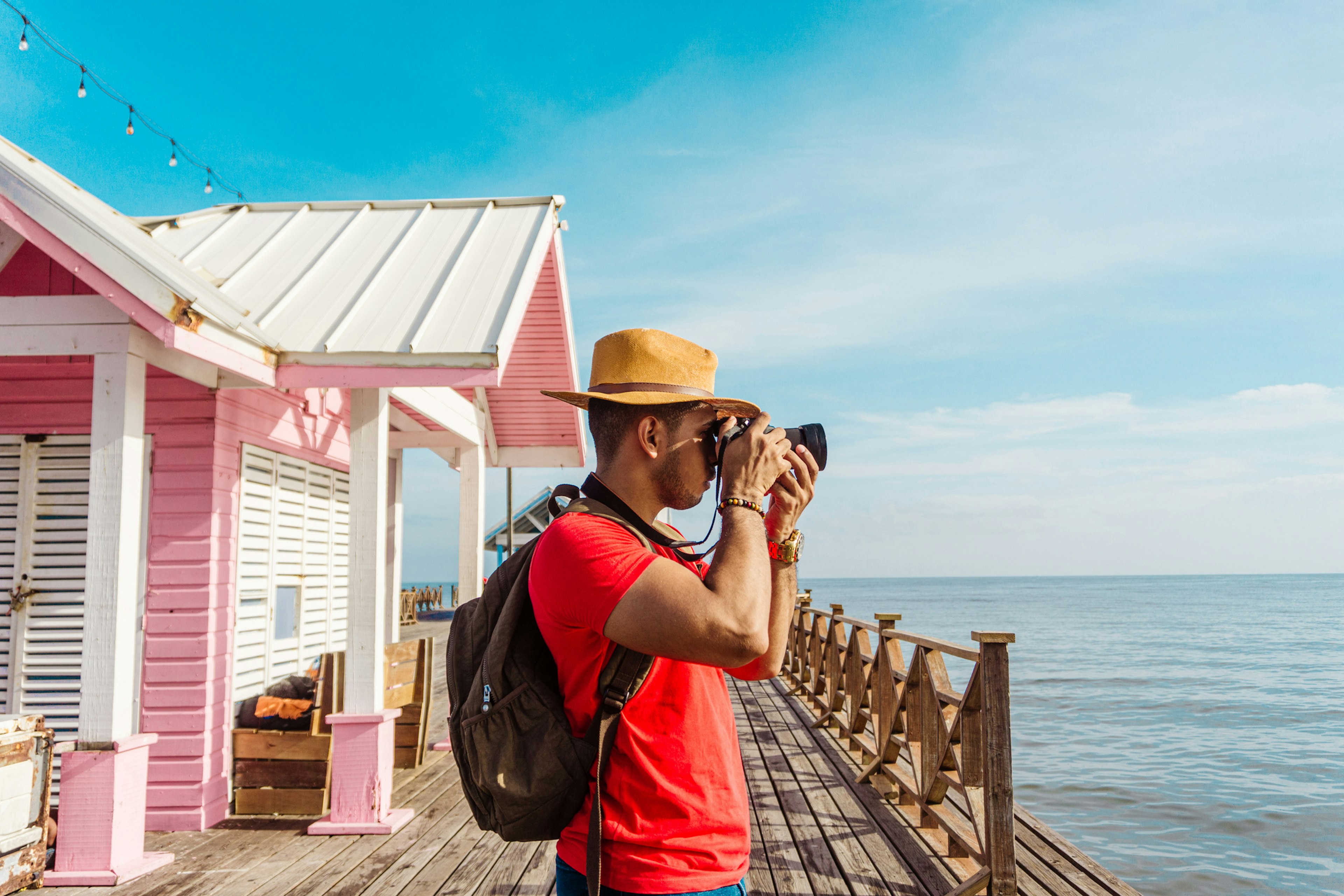 A man wearing a backpack taking pictures on the boardwalk in La Ceiba, Honduras