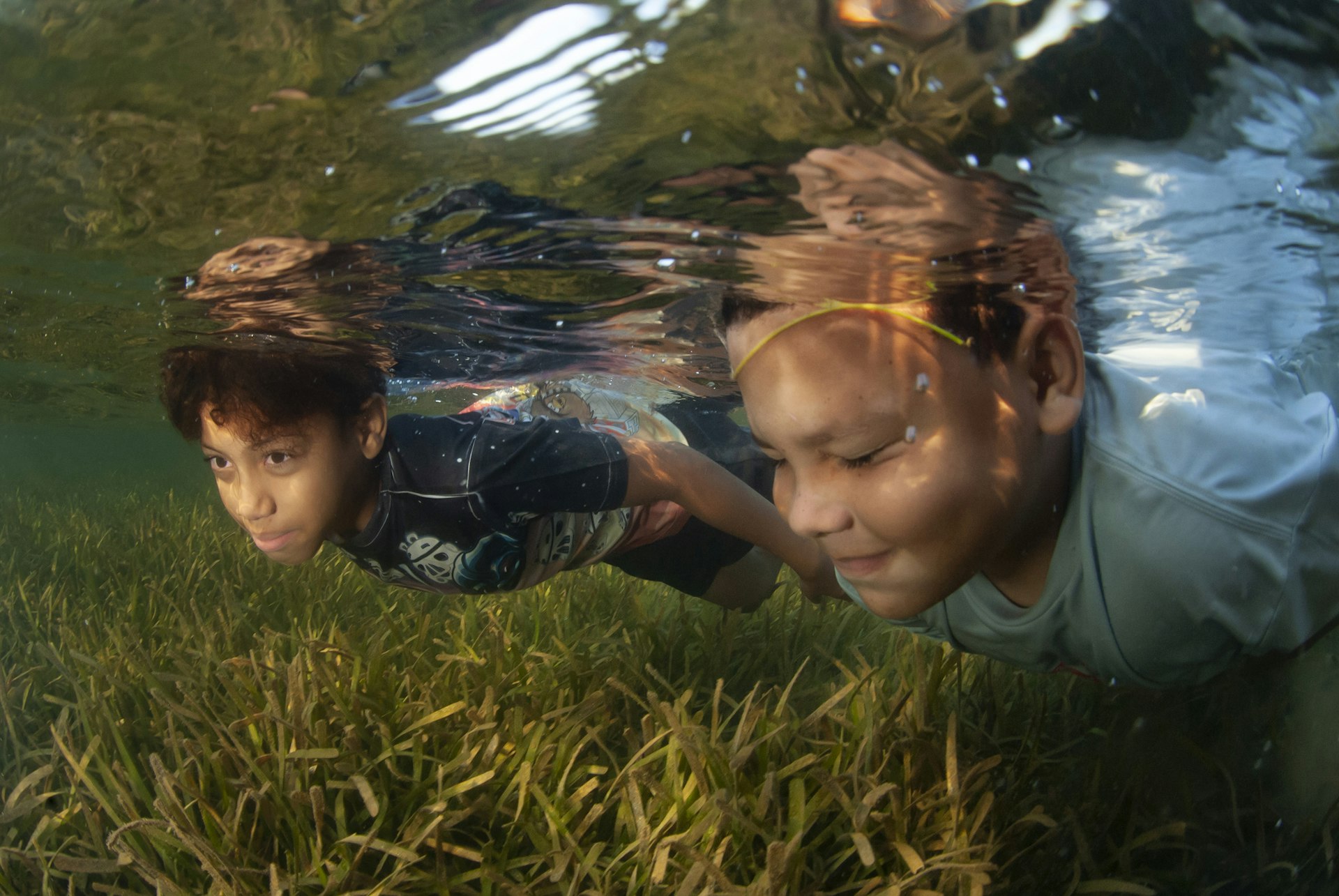Two boys swimming underwater over seagrass in Roatán, Honduras