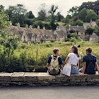 Three teenage kids enjoying summer vacations in Cotswolds, Gloucestershire, United Kingdom. ..They are sitting by the river and looking at the famous row of houses in Bibury...Shot with Canon R5
1667990110