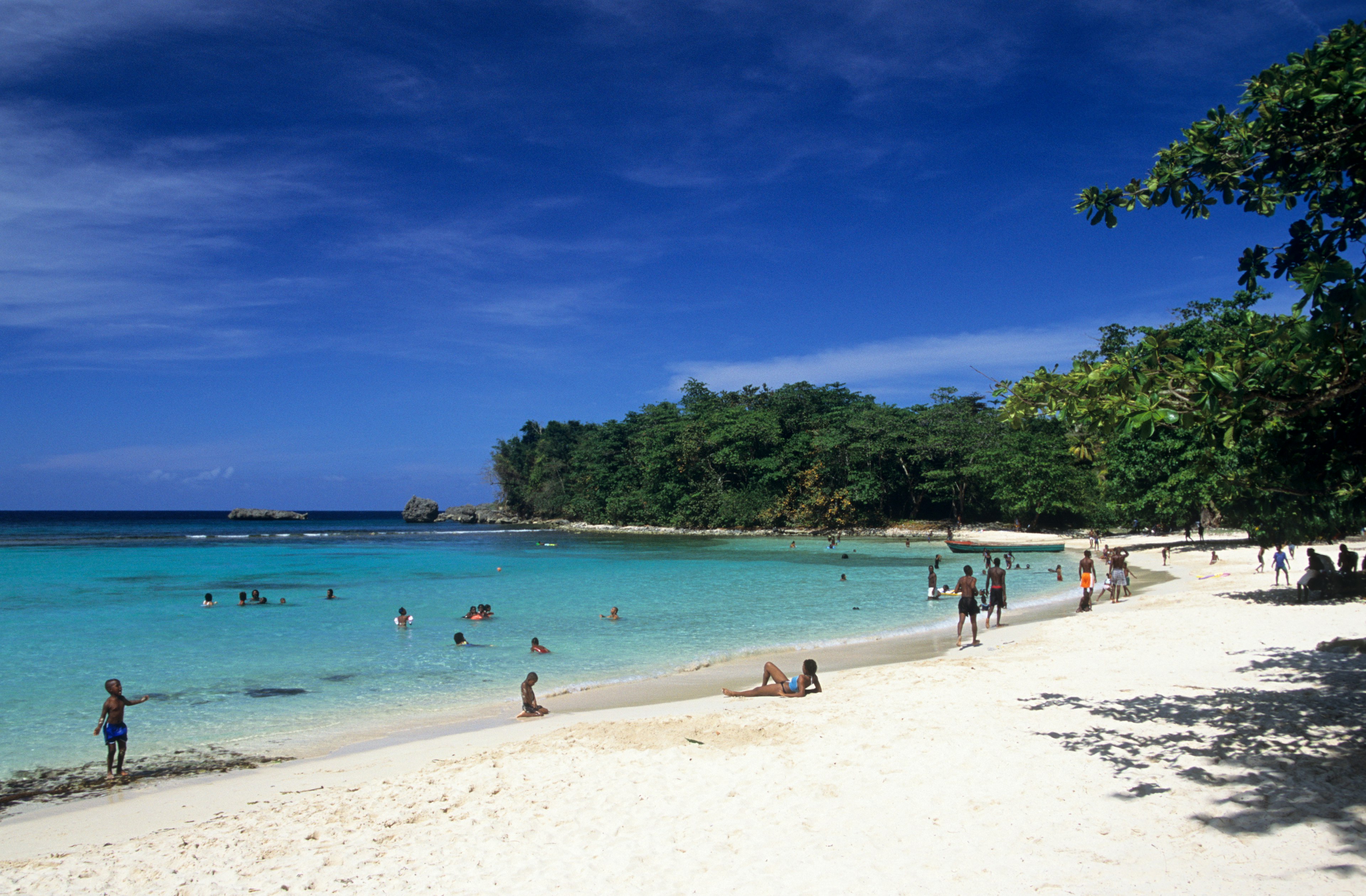 People lounging on the white sand beach and swimming in turquoise water at Winnifred Bay in Port Antonio, Jamaica