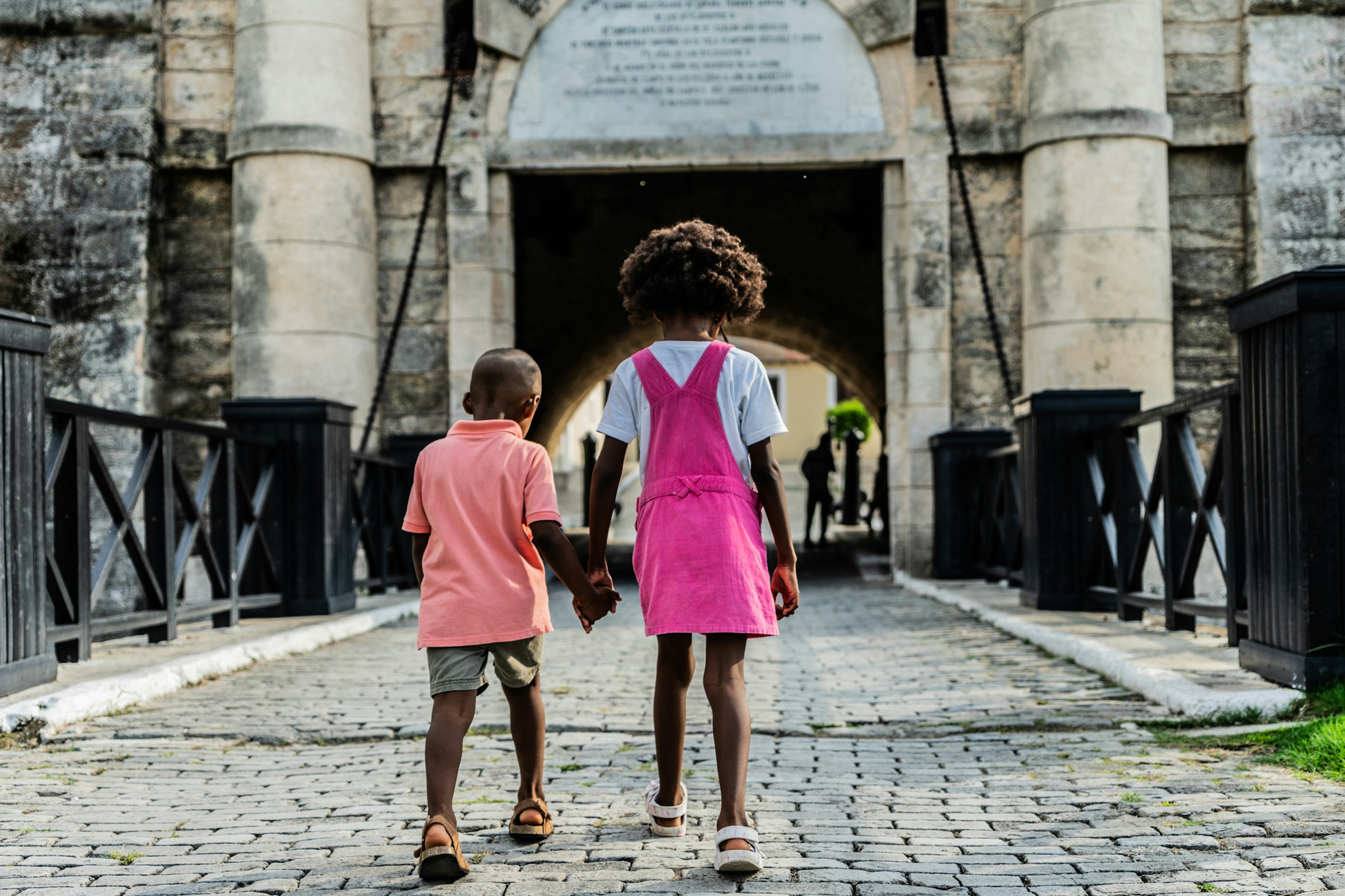 Rear view of siblings walking across a bridge towards a fort building