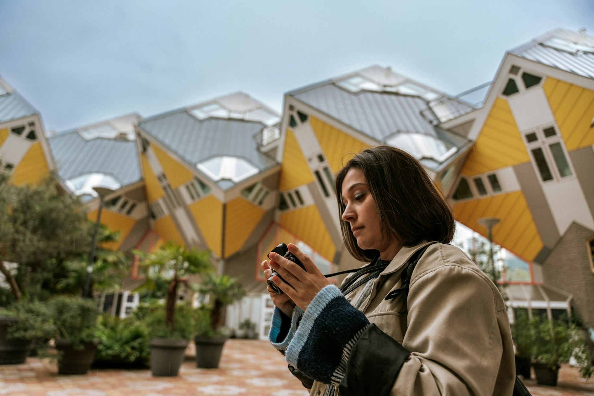 A woman with a camera in front of the yellow cube-like houses of the Overblaak Development, Rotterdam, the Netherlands
