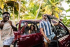 Three friends jumping with happiness next to their car with palm trees in the background