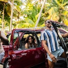Three friends jumping with happiness next to their car with palm trees in the background