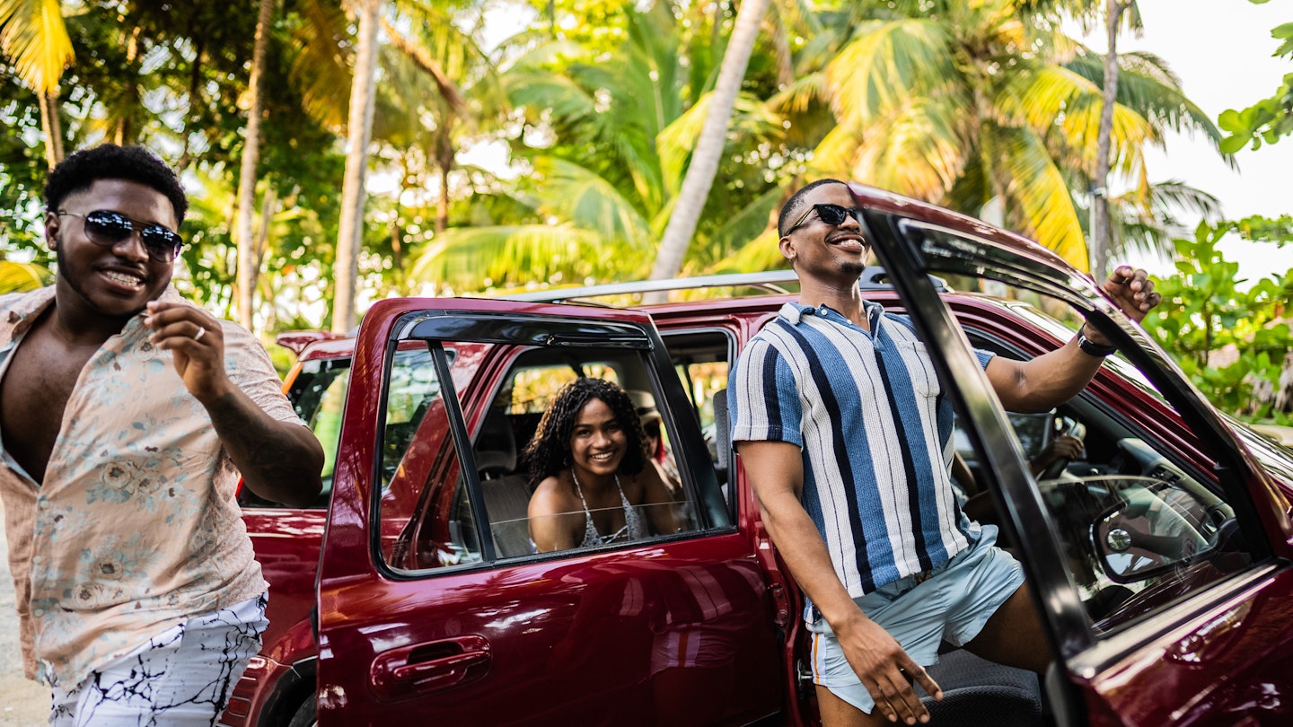 Three friends jumping with happiness next to their car with palm trees in the background