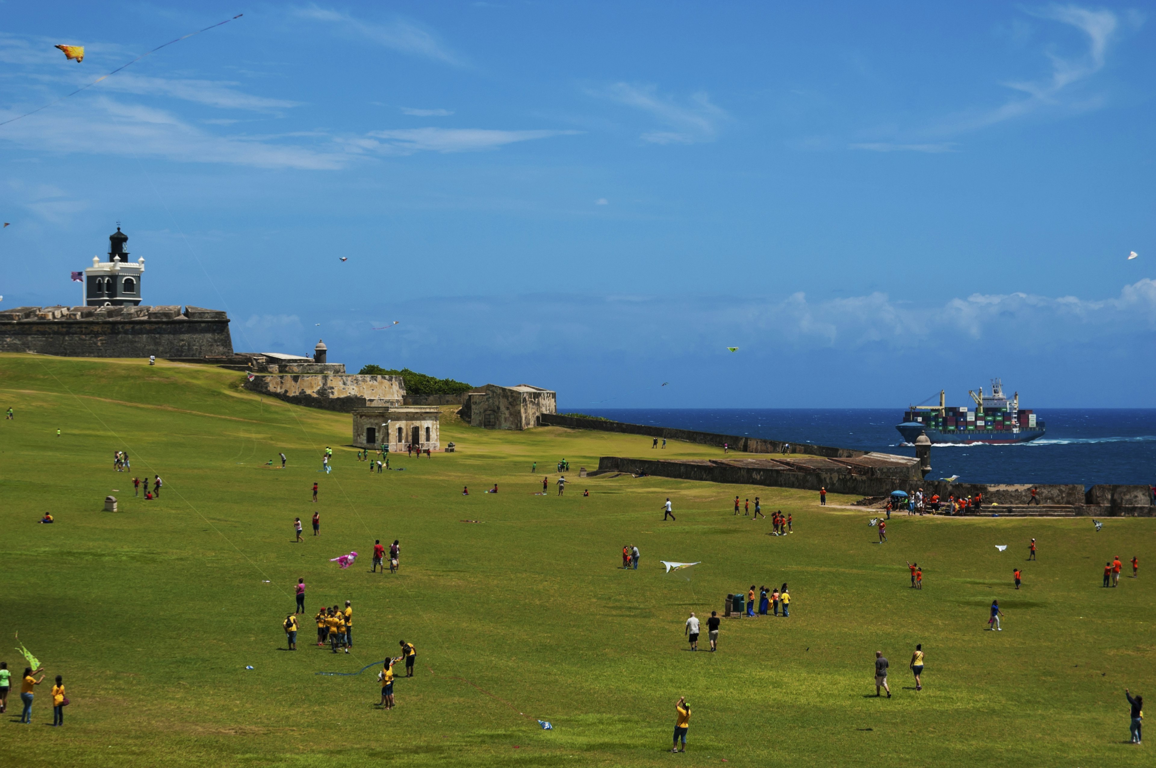 Children and parents are playing with kites in front of a seaside fortress