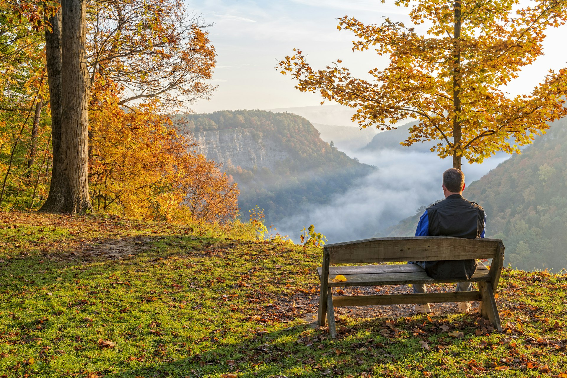 A man sitting on a bench enjoying an early morning sunrise at Letchworth State Park