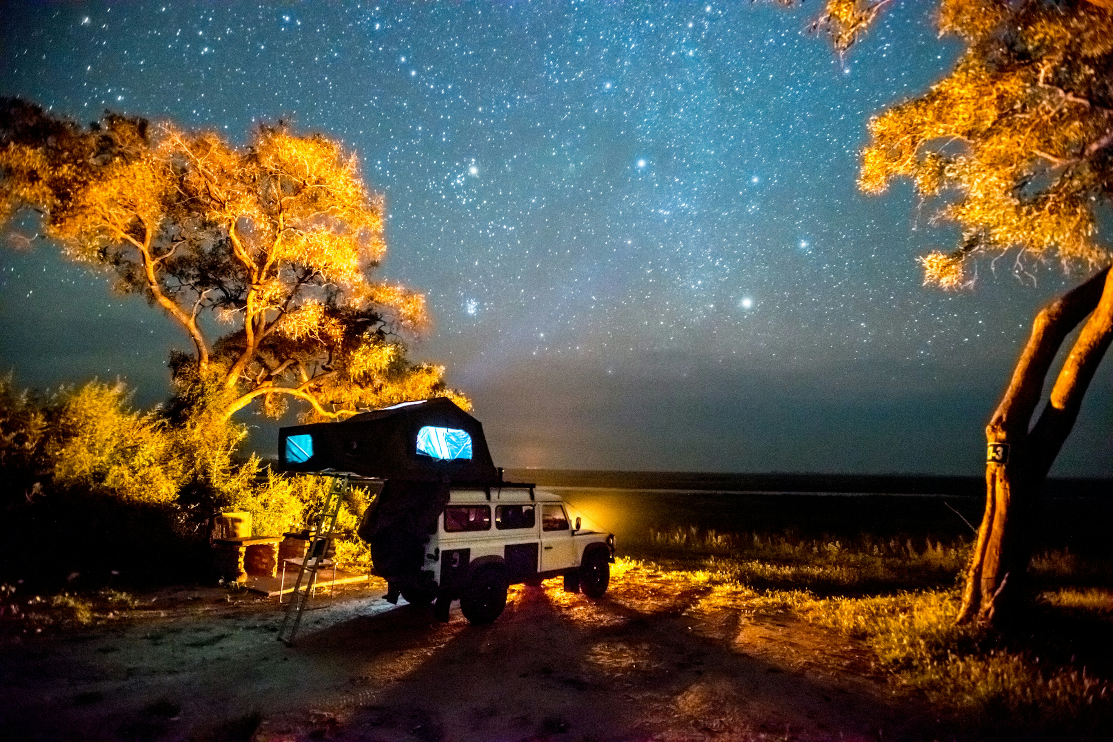 Under a blanket of stars, a 4WD camping car is next to a tree in Chobe National Park, Botswana.