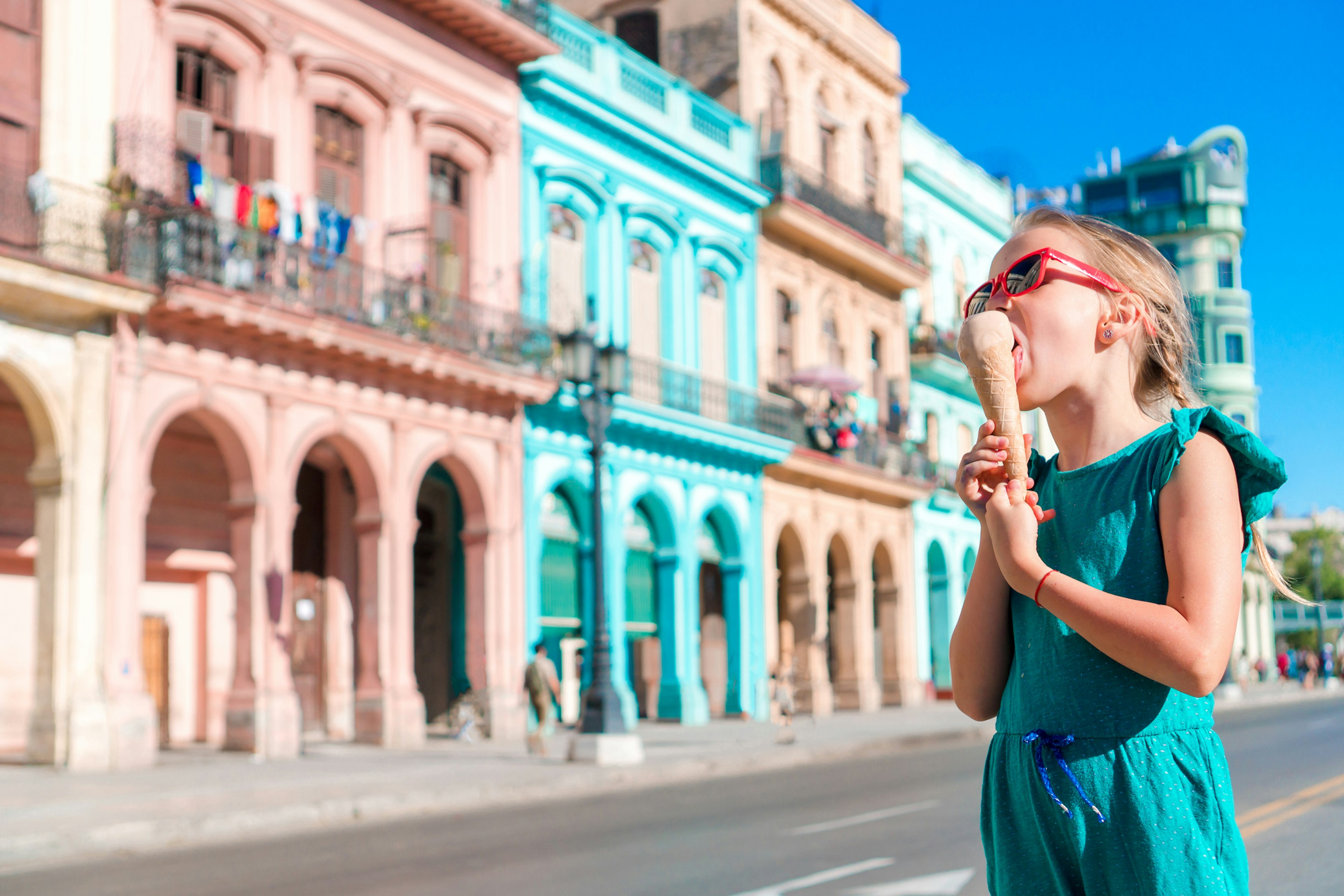 A child eats an ice cream in the street in front of some pastel-colored buildings