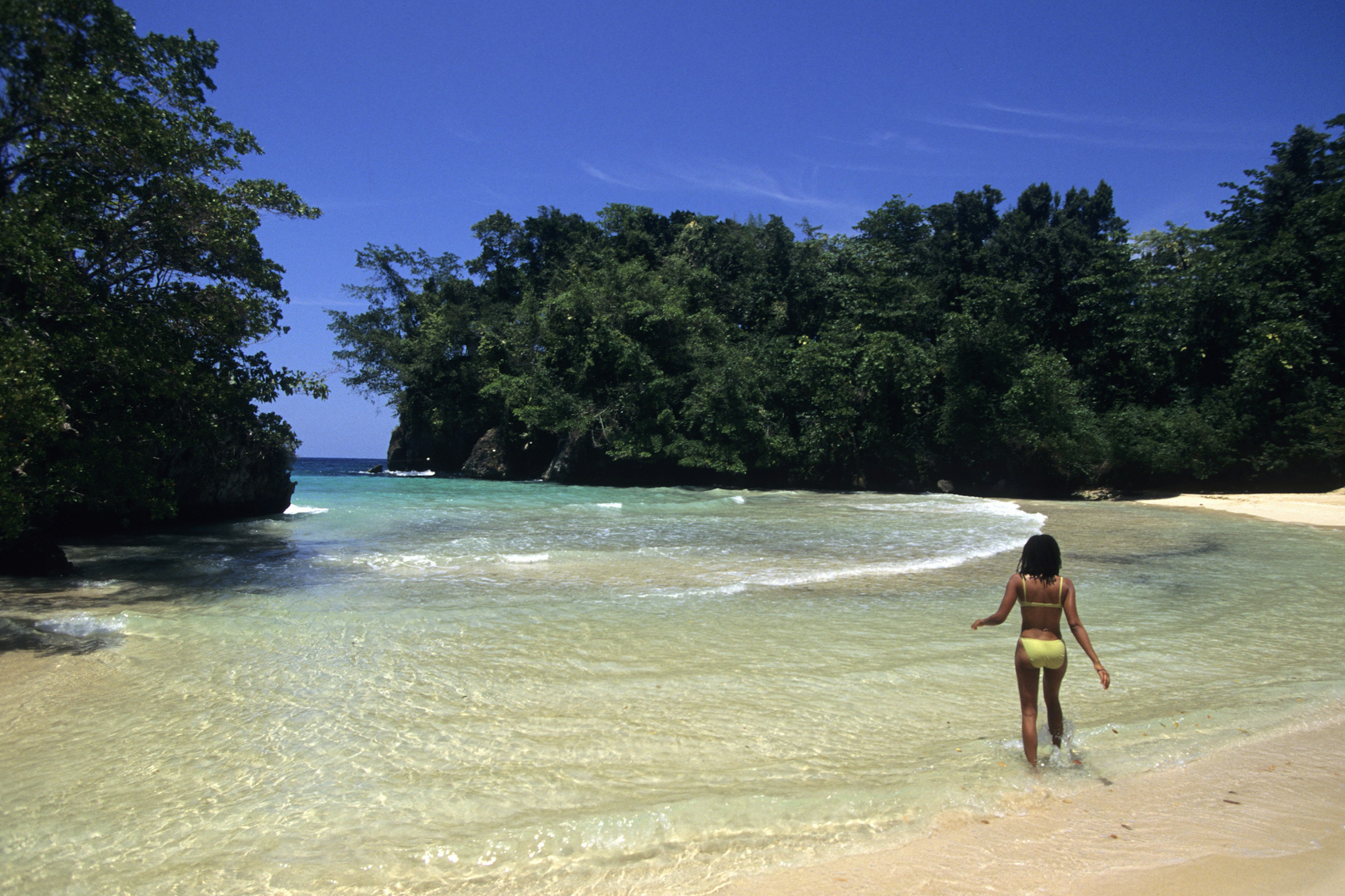 A woman in a yellow swimming costume walks into the water at Frenchman's Cove Beach, Jamaica