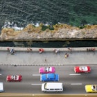 Large group of vintage American cars speeding along the Malecon in Havana, Cuba, motion blur, people sitting on sea wall, Caribbean Sea is visible in the background, elevated view.
993970062