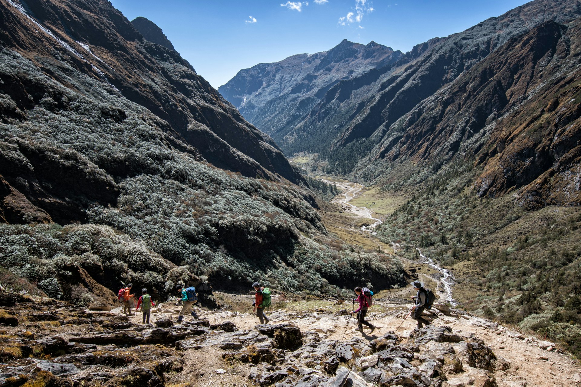 A group of hikers carry their gear on a trail through a mountainous region